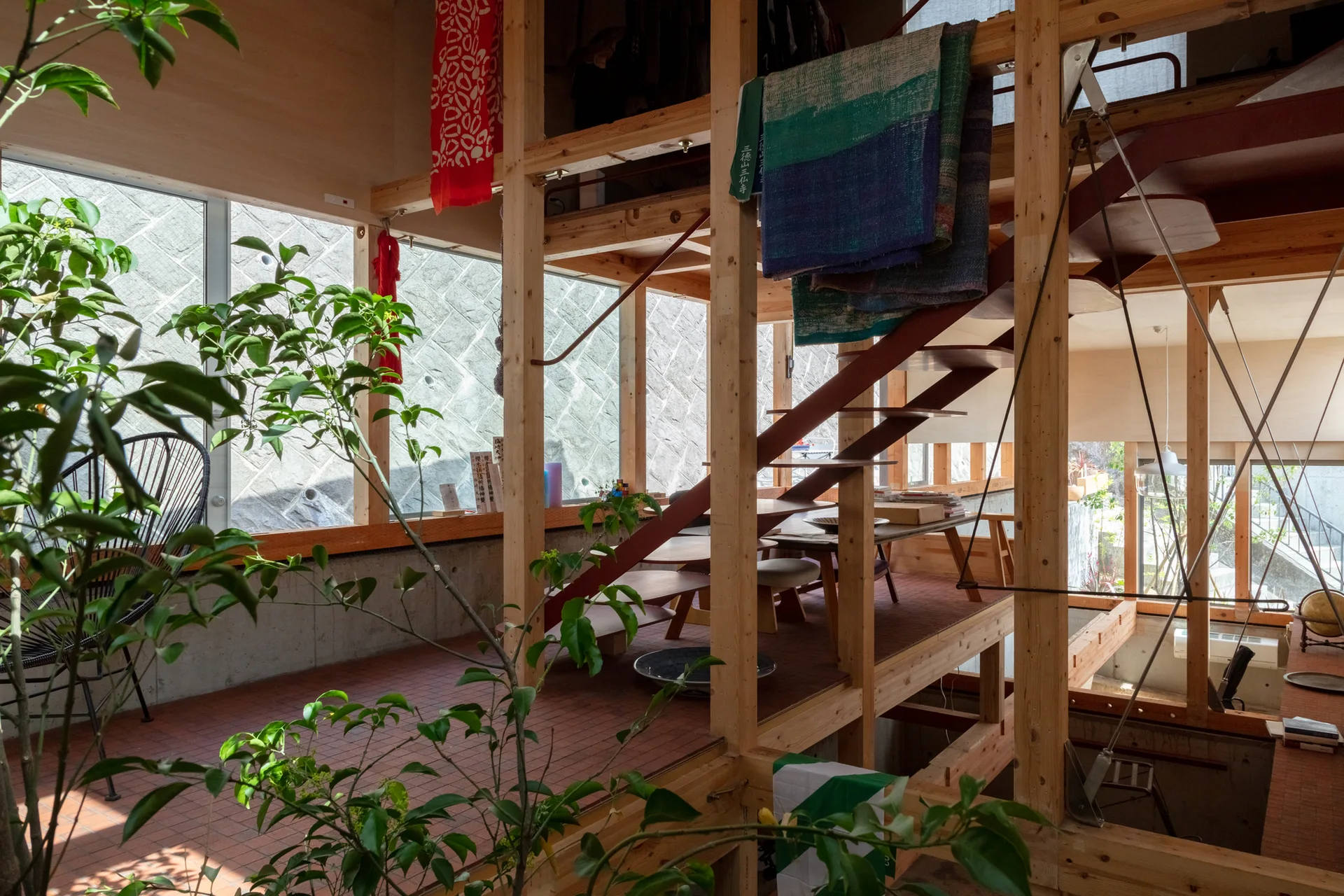 An open residential interior featuring exposed timber post-and-beam framing, a central wooden staircase, and a raised platform with a seating area.