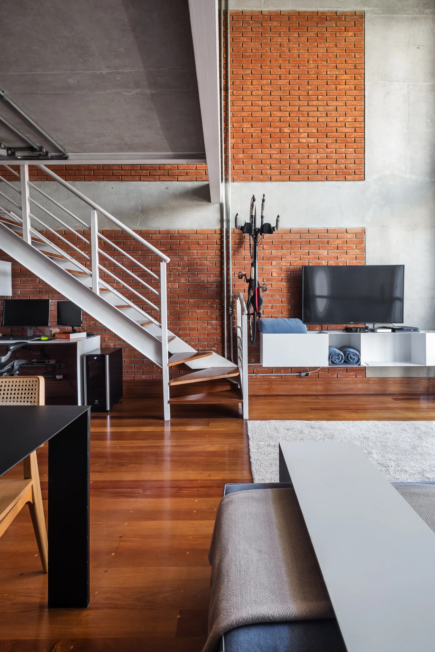 An industrial loft living room features an exposed brick wall, a white metal staircase with wood treads, and a floating white media console.