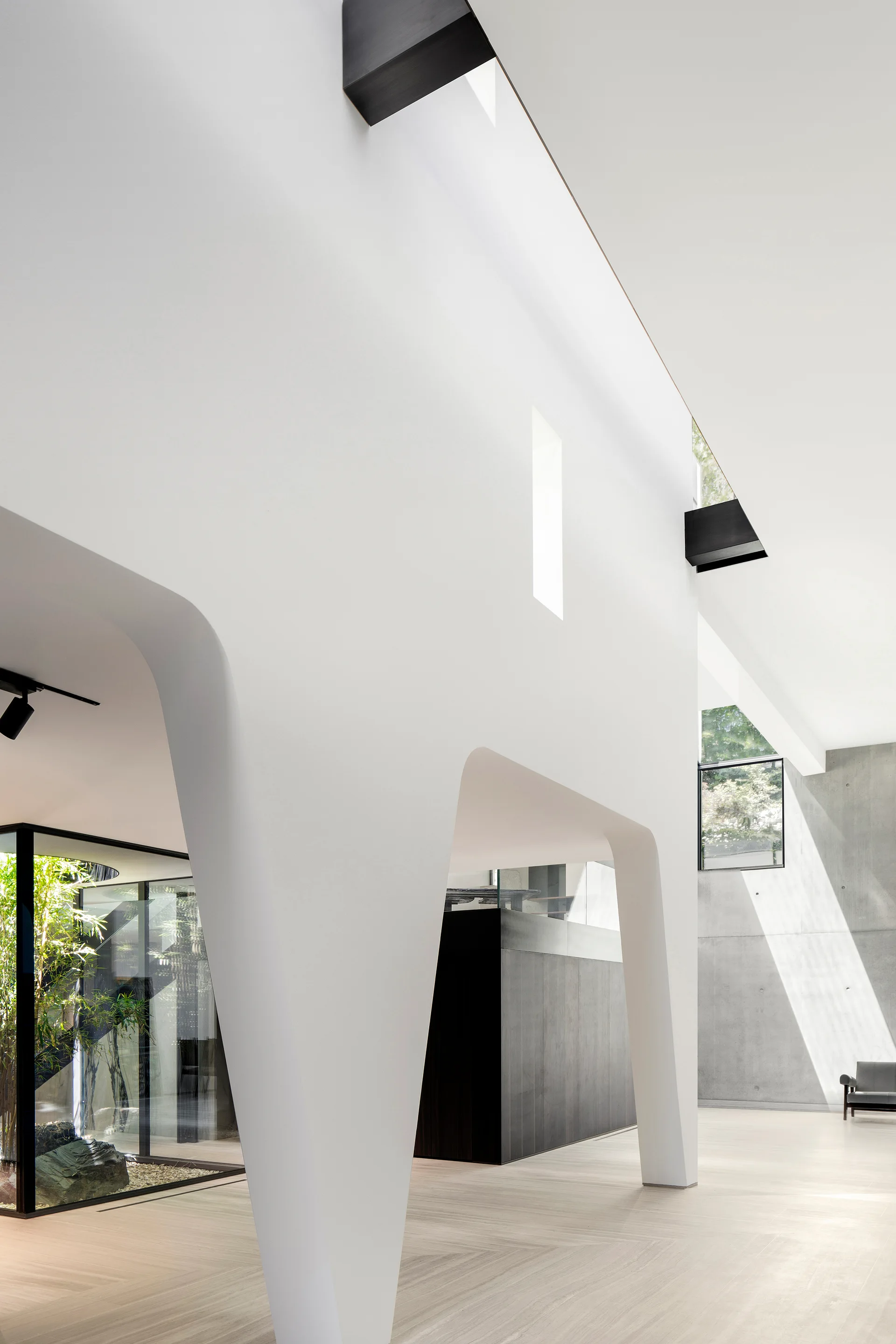 A spacious minimalist interior featuring a large white sculptural plaster arch, light wood floors, and smooth concrete walls.