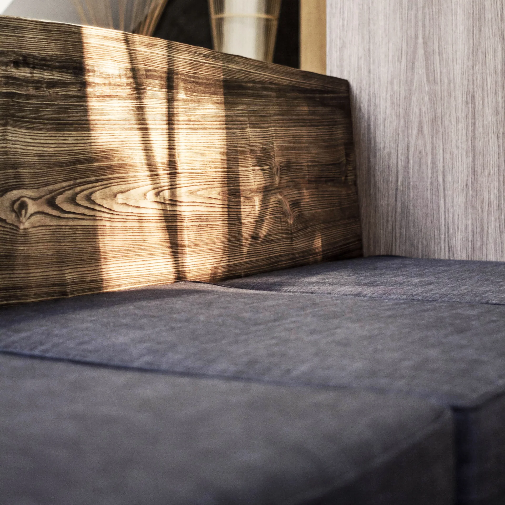 A close-up of dark gray fabric upholstery next to a thick wood ledge with a prominent natural grain and light vertical wall paneling.