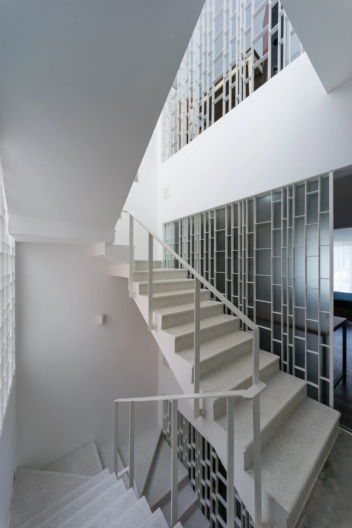 A multi-level white staircase with speckled stone steps, thin metal railings, and a tall geometric metal grid partition.