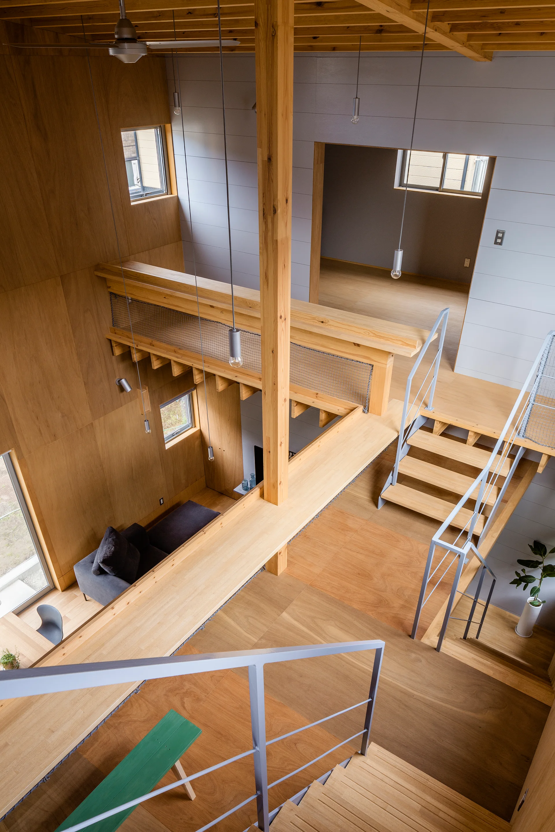 An overhead view of a multi-level wooden home featuring plywood-paneled walls, an open staircase with grey metal railings, and hanging pendant lights.