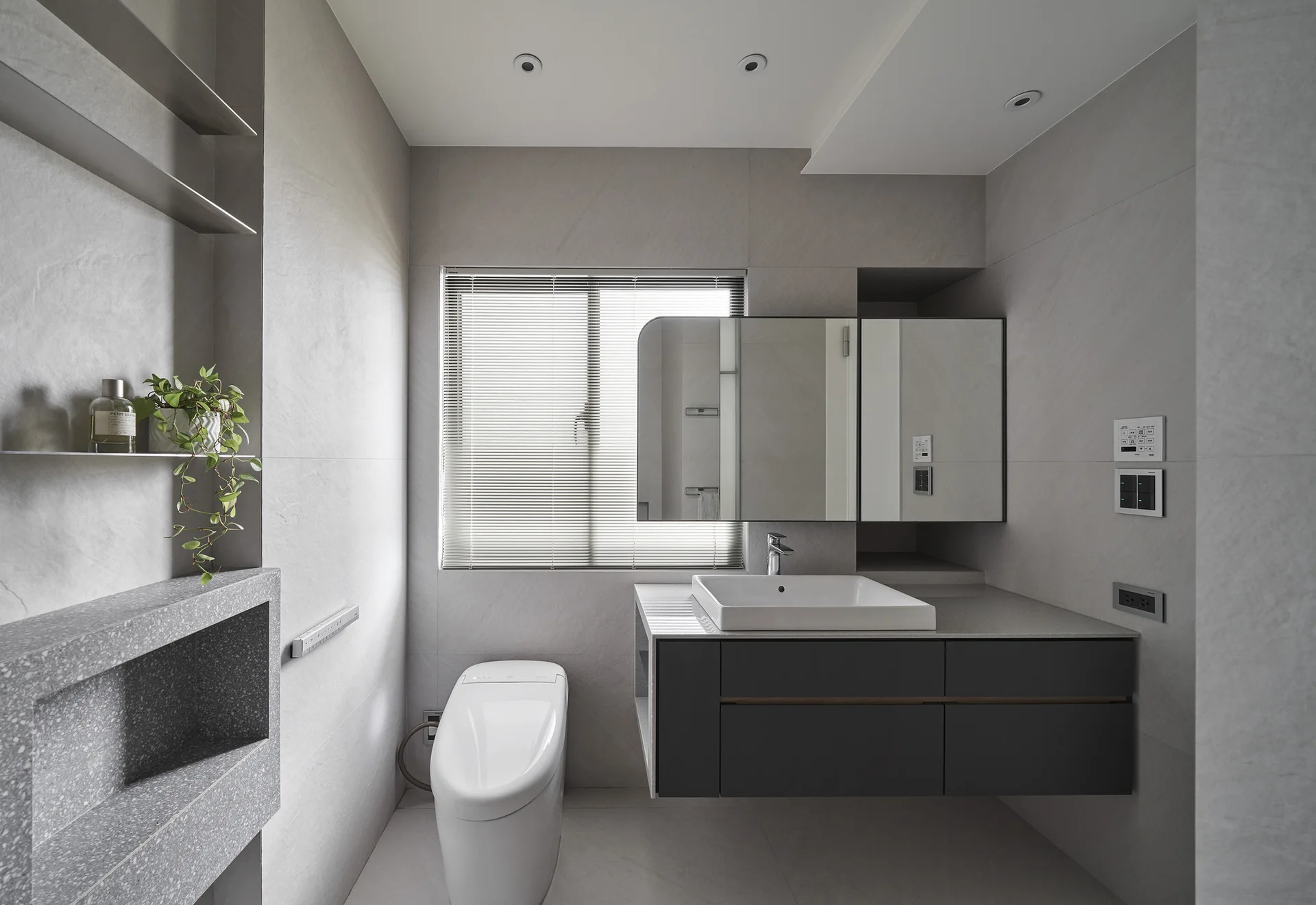 A minimalist modern bathroom featuring gray tiled walls, a floating charcoal vanity with a white vessel sink, and a modern toilet.