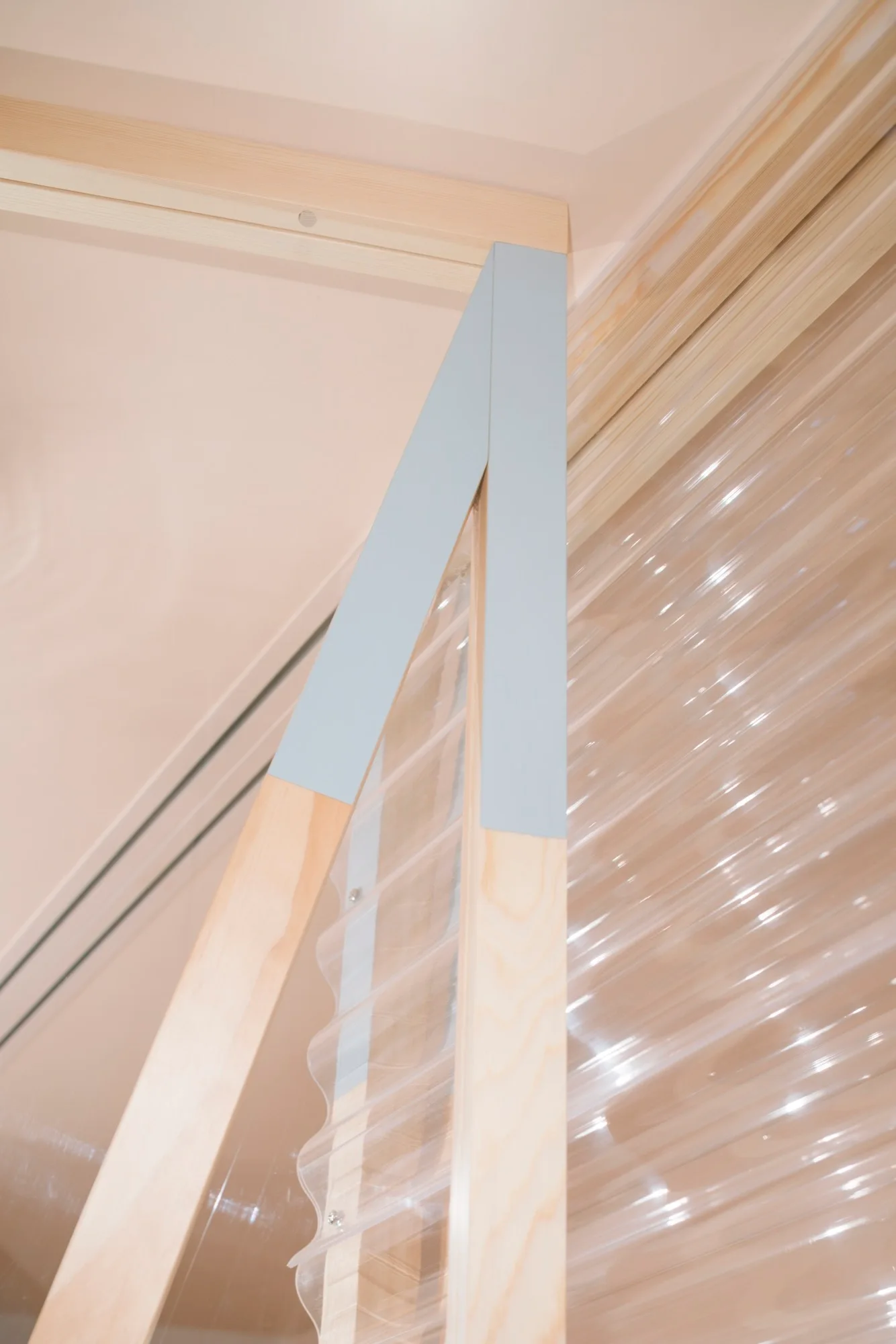 Architectural detail of a light wood support frame with a pale blue painted section and a transparent corrugated panel.