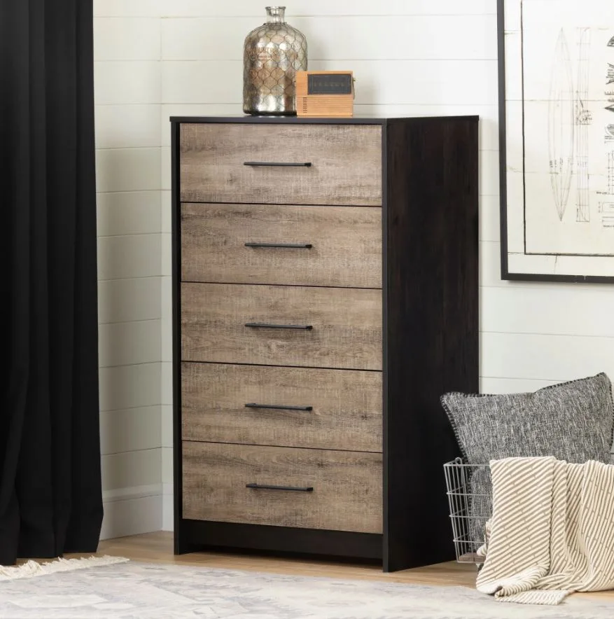 A tall five-drawer bedroom dresser with a dark brown frame and lighter wood grain drawer fronts stands against a white paneled wall.