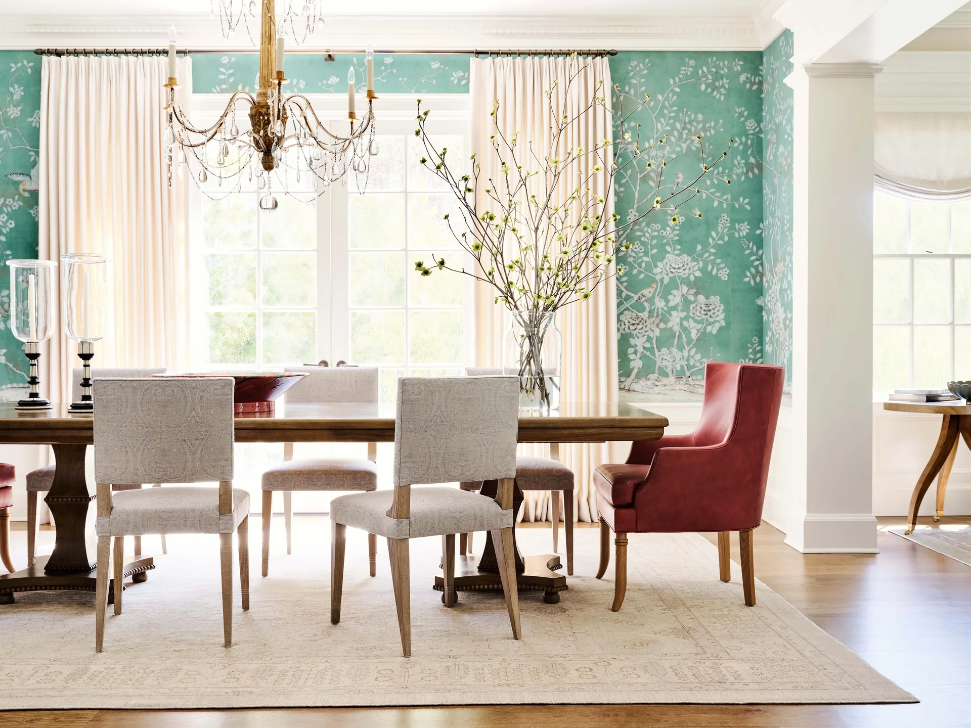 A formal dining room features a wood table with patterned chairs, a red host armchair, and bright green floral wallpaper.