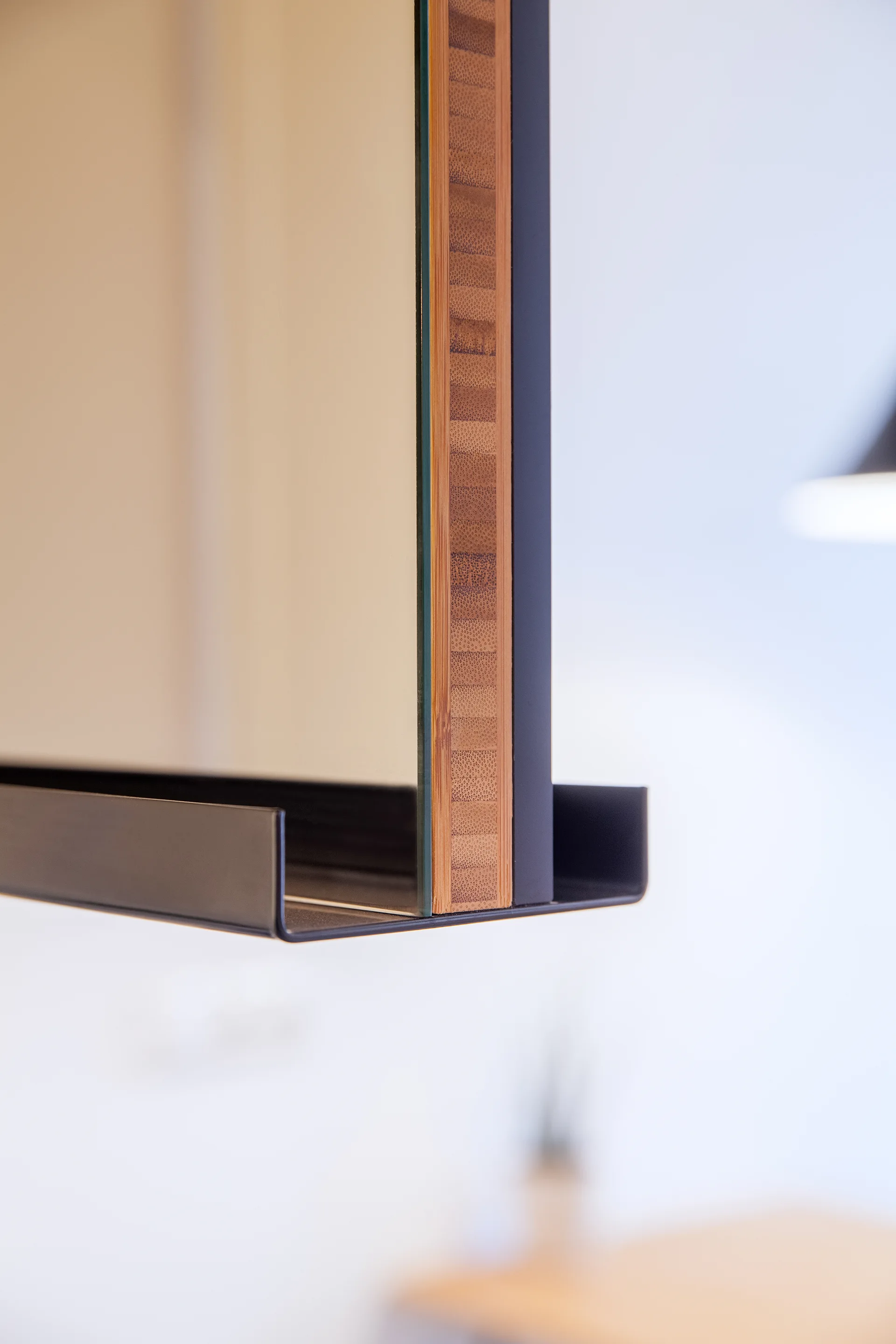 An extreme close-up of a modern mirror showing its layered bamboo edge, reflective glass, and a matte black metal bottom shelf.