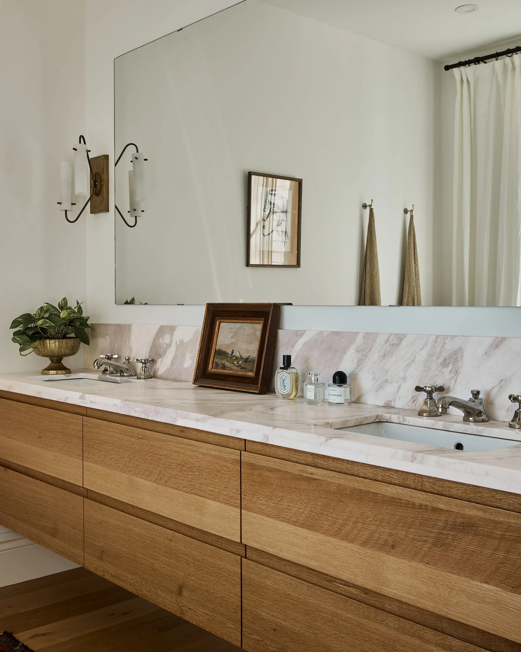A modern floating wood vanity with double sinks, a veined marble countertop, a slab backsplash, and a large frameless mirror.