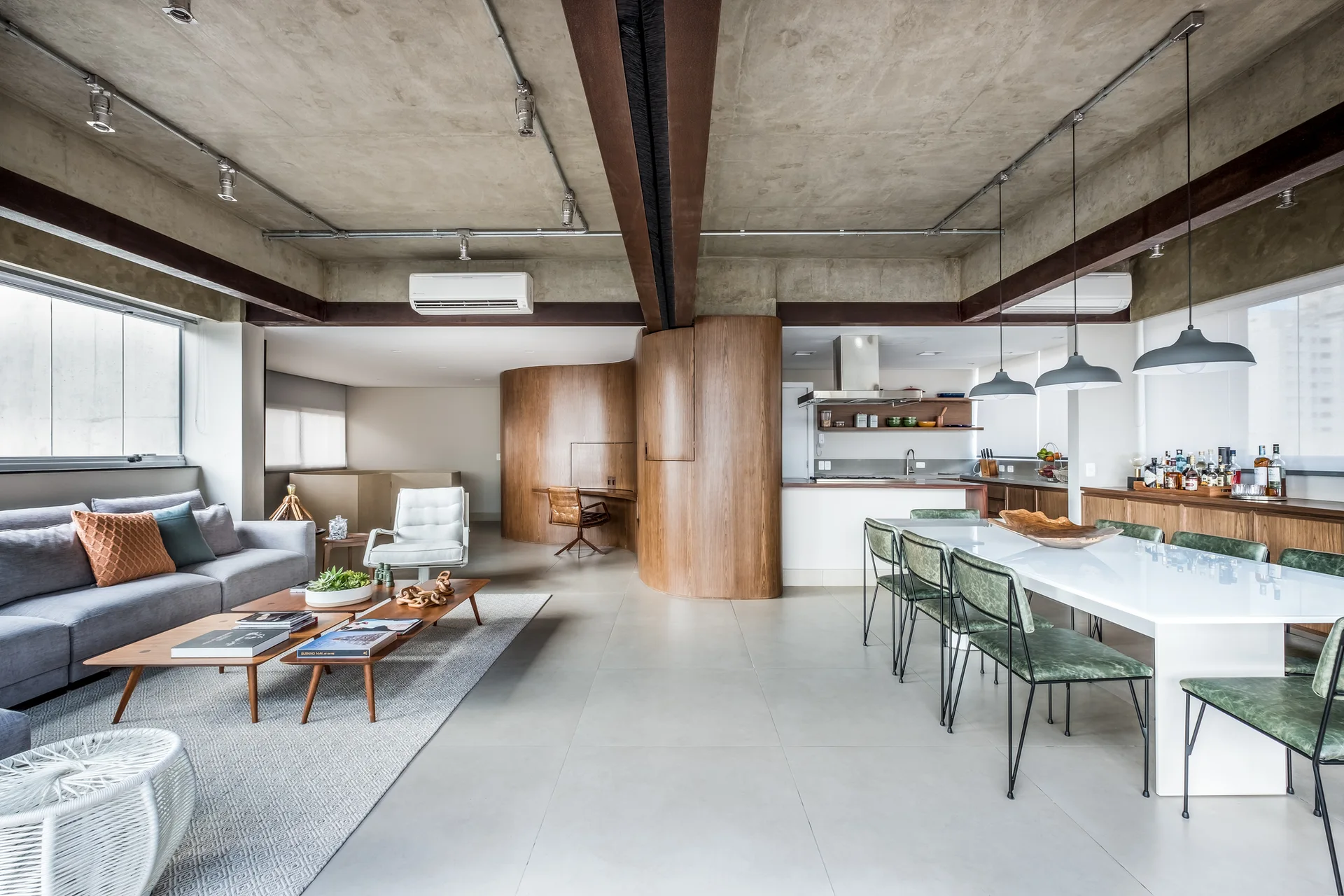 An industrial open-plan living and dining room featuring a raw concrete ceiling, a curved wood-paneled partition wall, a gray sofa, and a white dining table.