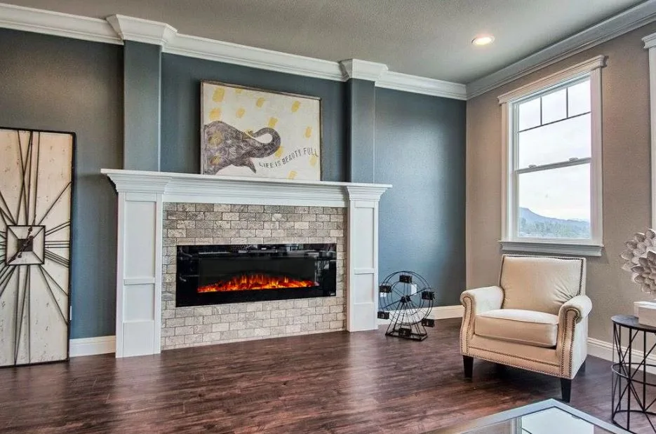 A transitional living room featuring a stone fireplace with a white wood mantel against blue-gray walls, alongside a cream armchair near a window.