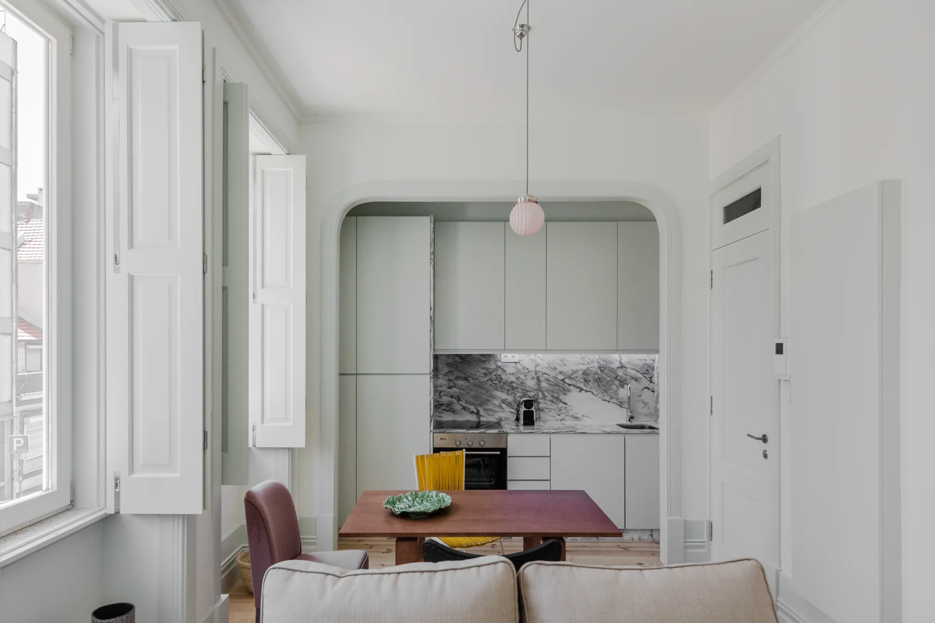 A modern dining area features a wooden table next to an archway opening into a kitchen with mint green cabinets and a marble backsplash.