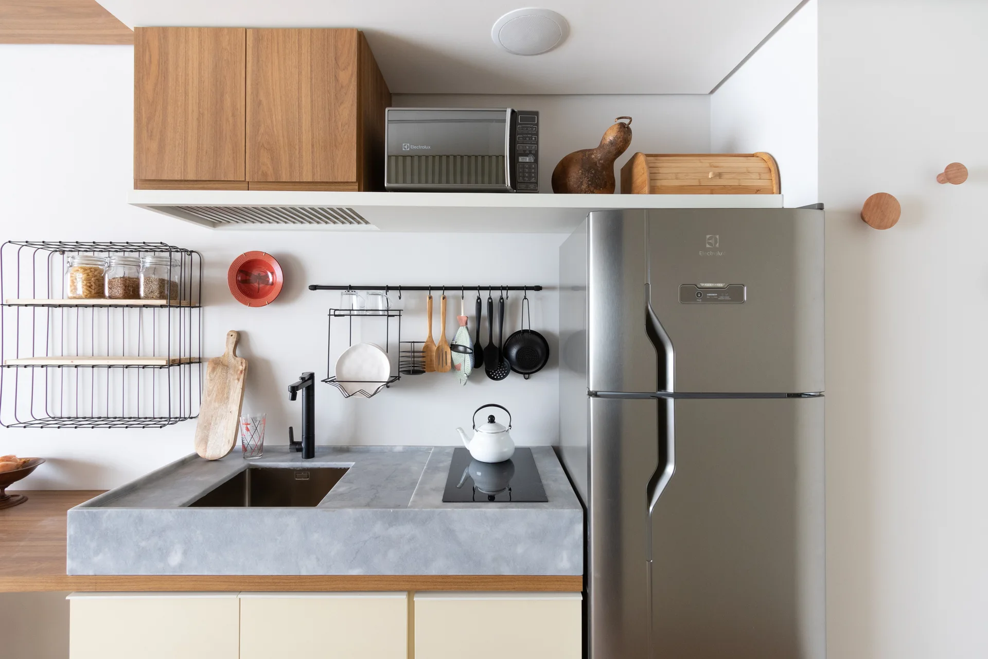 A compact kitchen features a thick grey stone countertop with an integrated sink, a stainless steel refrigerator, and natural wood upper cabinets.