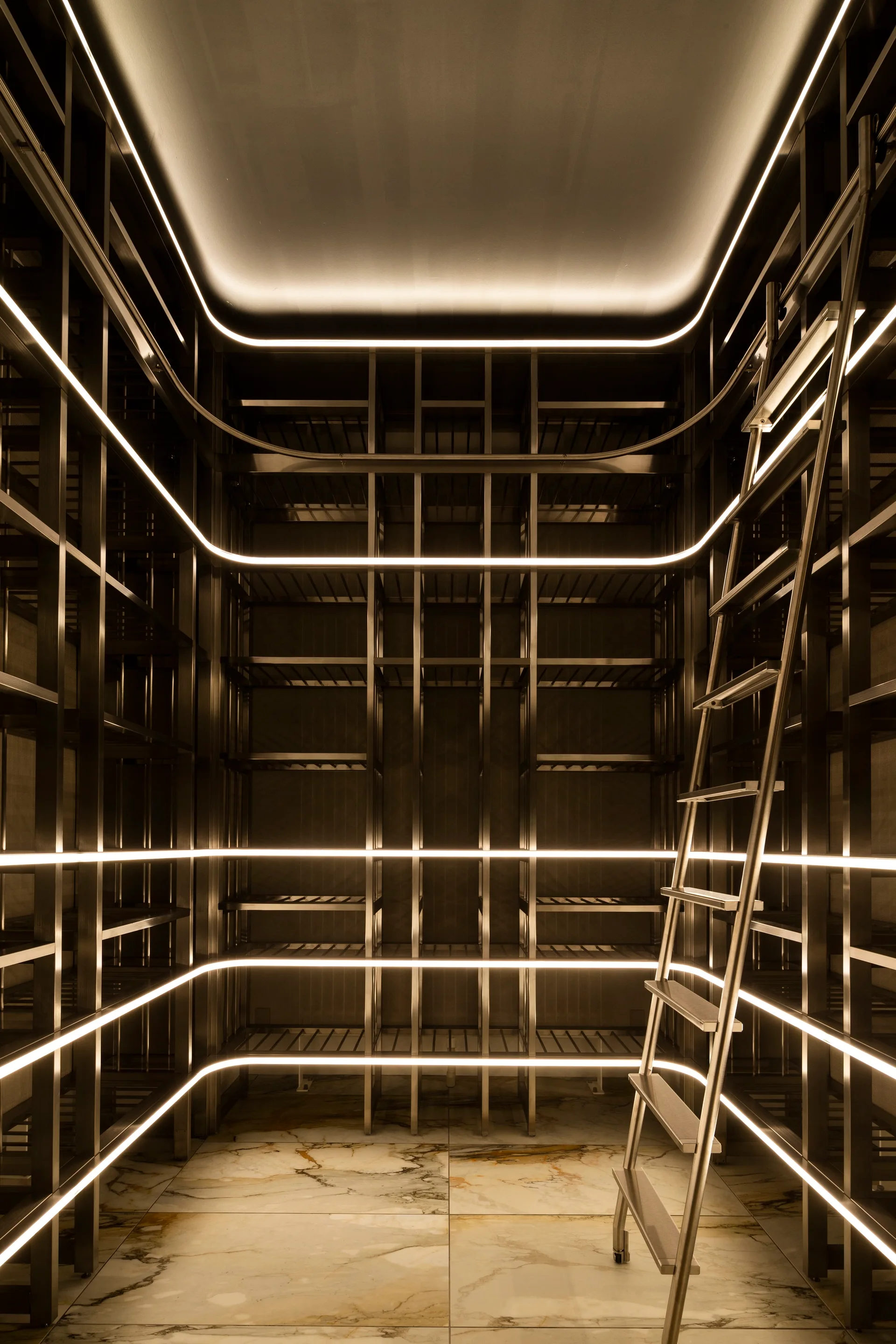 Symmetrical floor-to-ceiling dark bronze metal shelving units featuring integrated warm LED strip lights, a rolling ladder, and polished marble floor tiles.