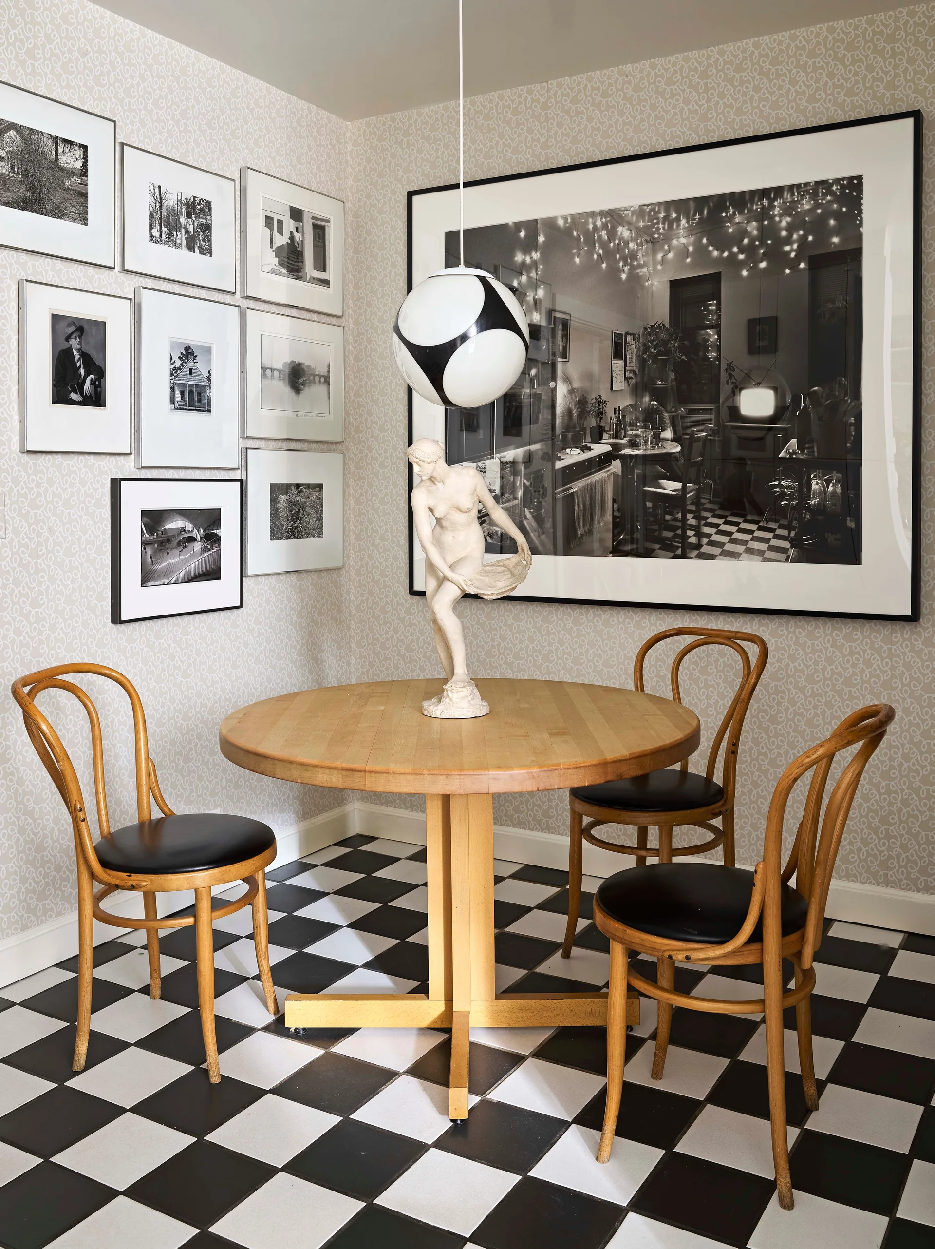 A corner dining area features a round wood table with bentwood chairs, set against swirling patterned wallpaper, a gallery wall, and checkerboard floor tiles.