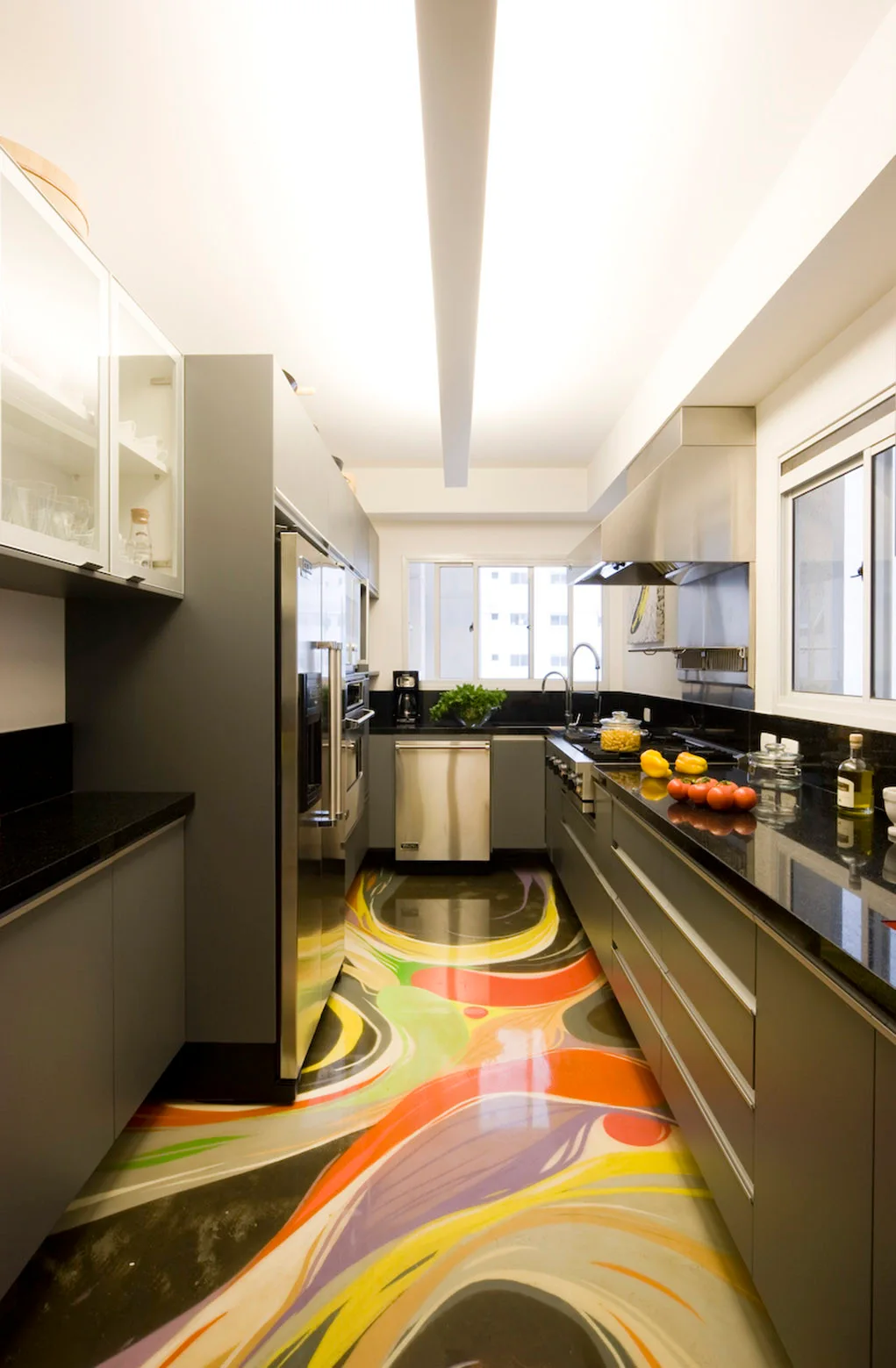A modern galley kitchen featuring matte grey cabinets, black countertops, stainless steel appliances, and a polished multicolored swirl pattern floor.