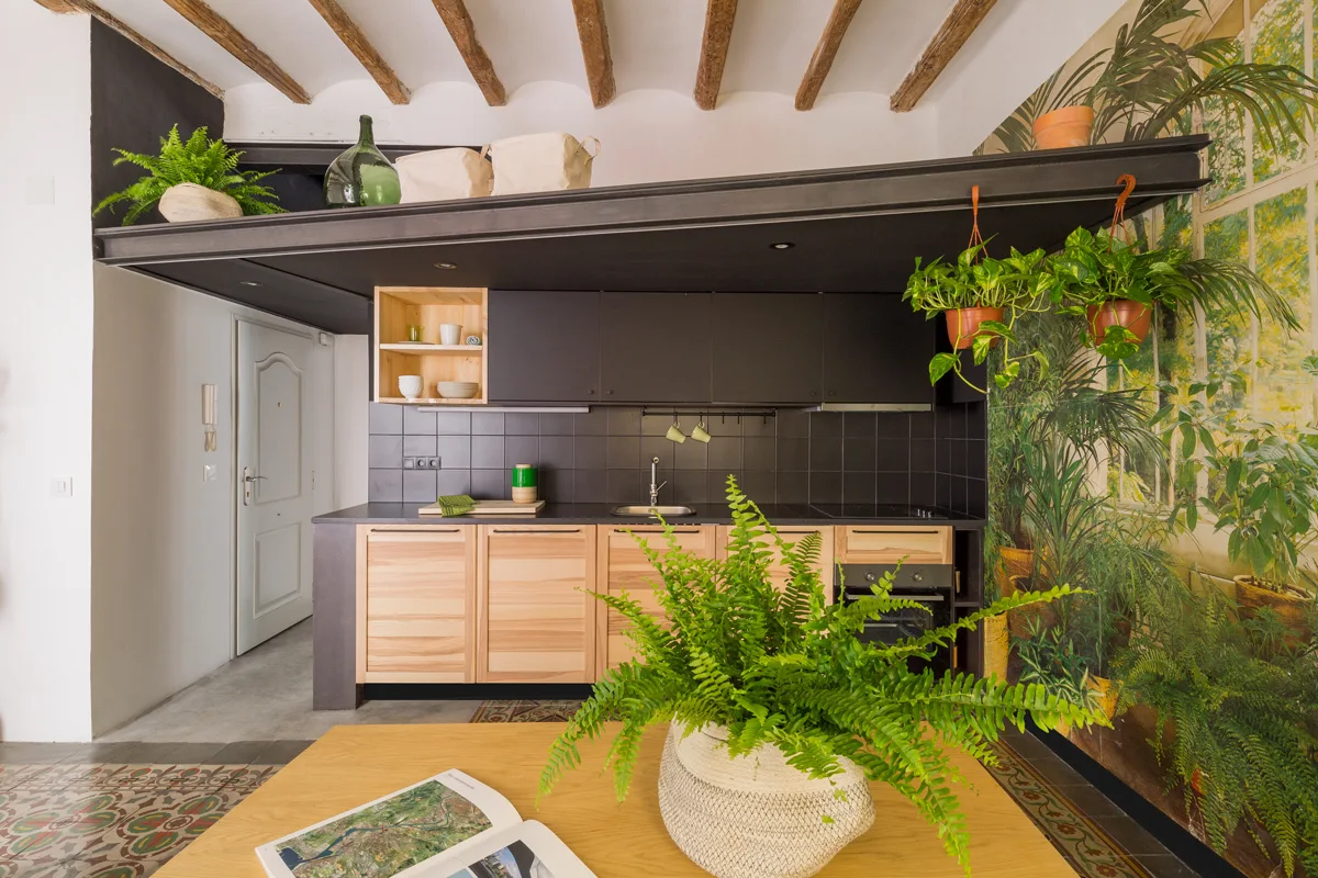 A modern kitchen features black upper cabinetry, natural wood lower cabinets, exposed wooden ceiling beams, and a large botanical wall mural.