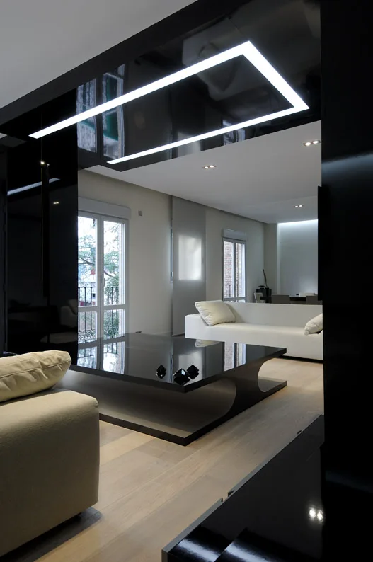 A minimalist living room features a glossy black coffee table and matching ceiling panel with a rectangular recessed light, white sofas, and wood floors.