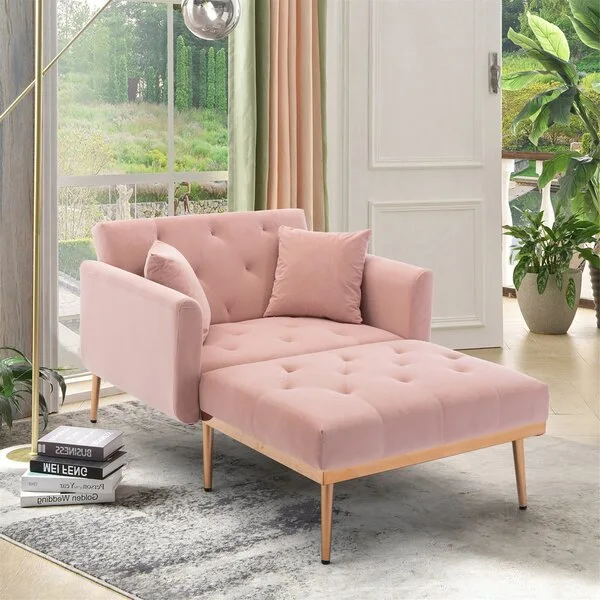A tufted blush pink velvet chaise lounge with tapered gold legs sits on a distressed grey rug near a large window.