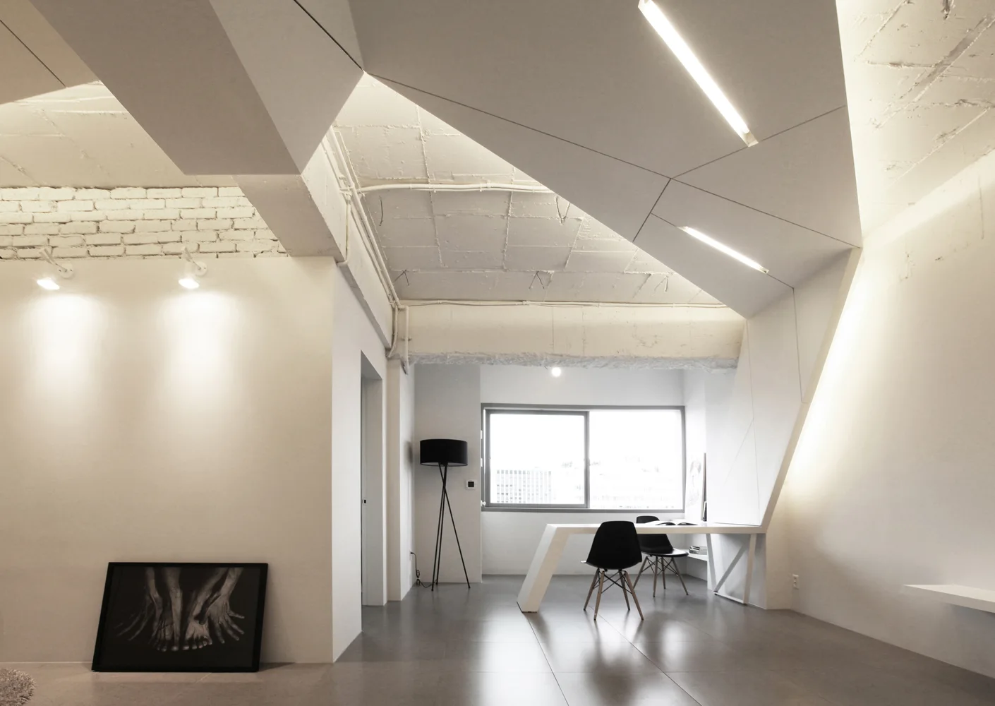 A minimalist home office features a white angular desk, black chairs, and an angled ceiling with integrated linear lights.