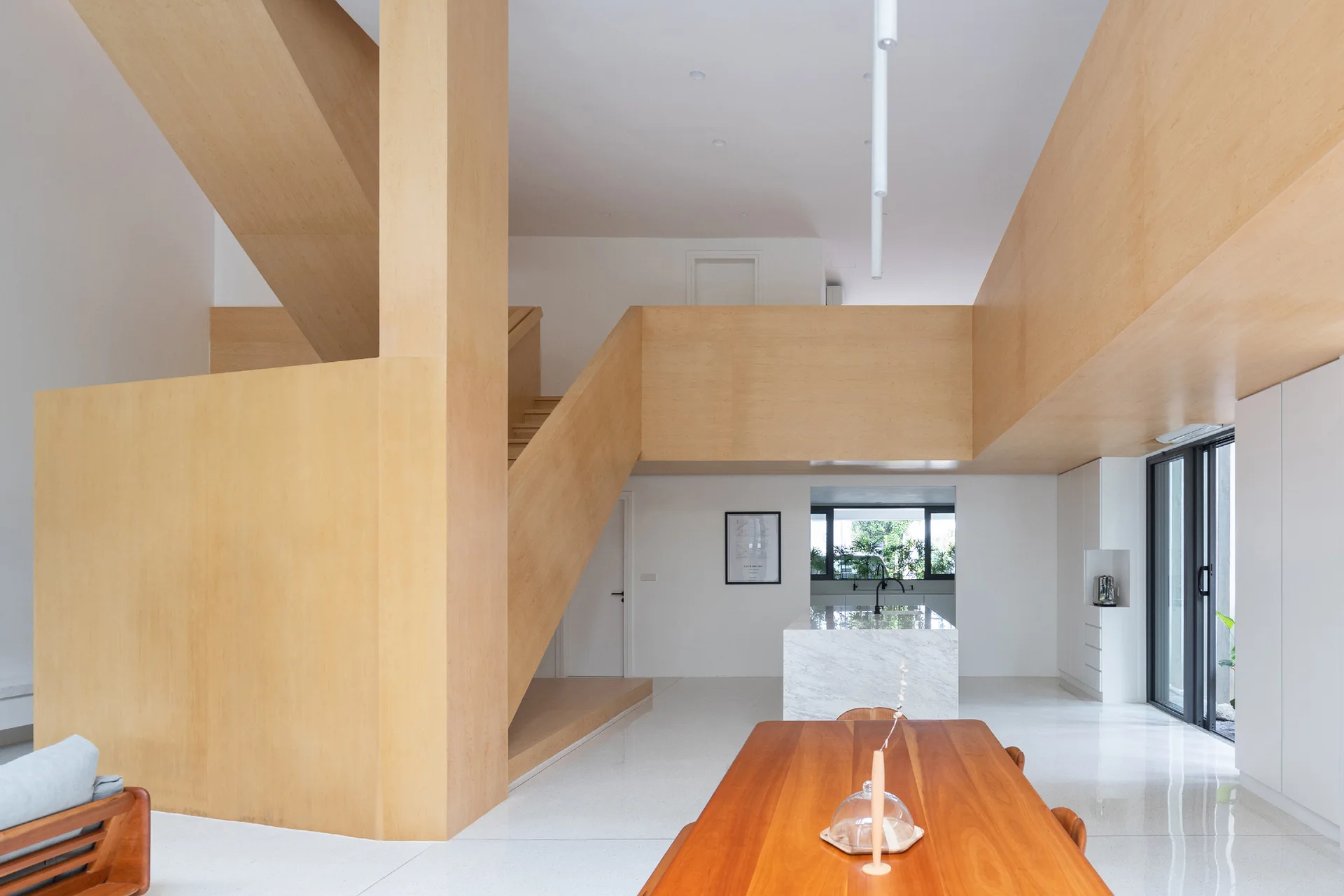 An open-concept home featuring a massive light wood-clad staircase structure next to a wooden dining table and a marble kitchen island.