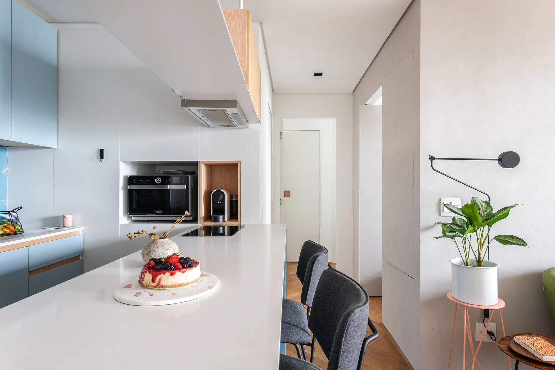 A modern kitchen with a white breakfast island, light blue cabinetry, built-in wall appliances, and herringbone wood floors.