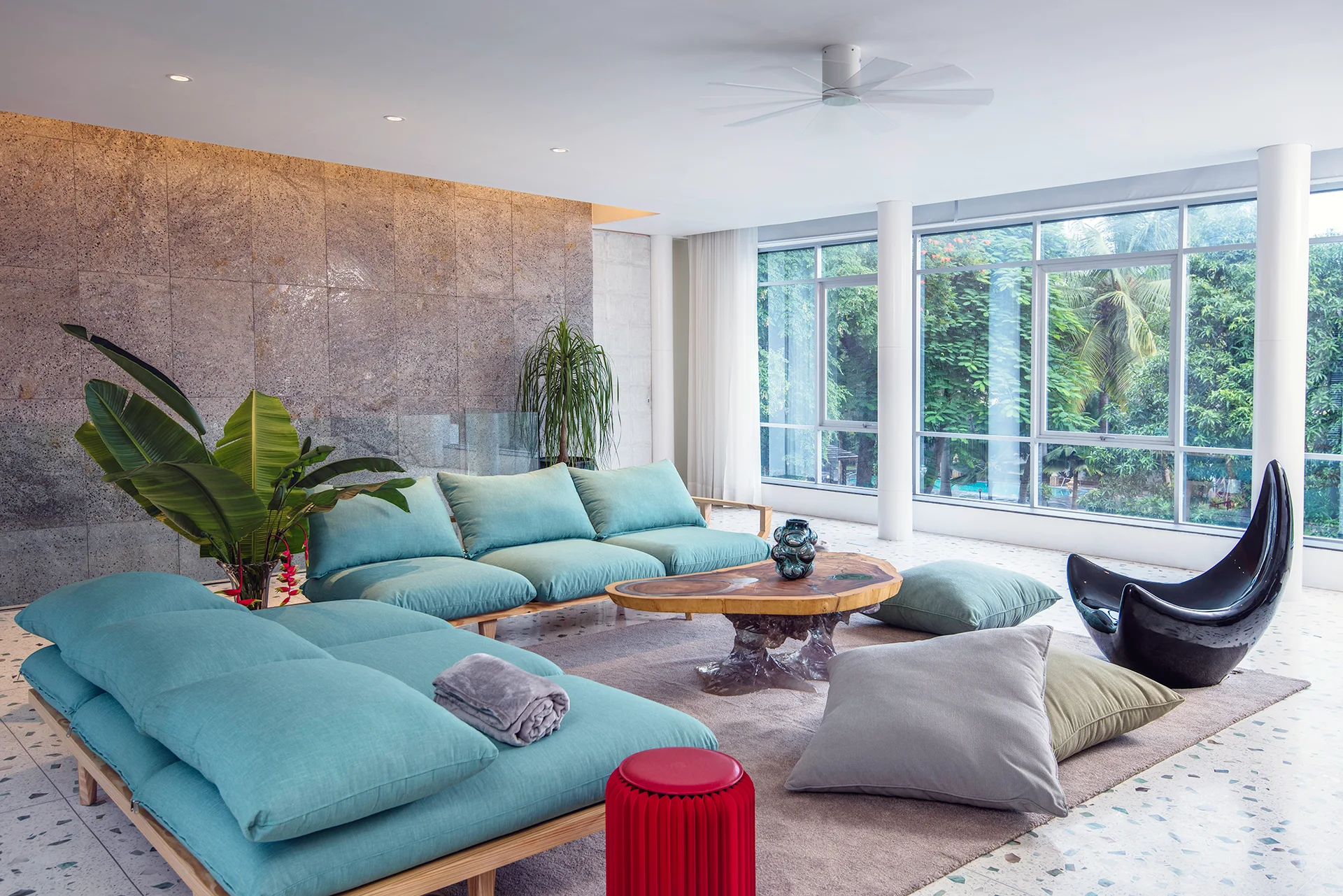 A spacious living room features low-profile light blue modular sofas, a live-edge wood coffee table, speckled terrazzo floors, and a stone accent wall.
