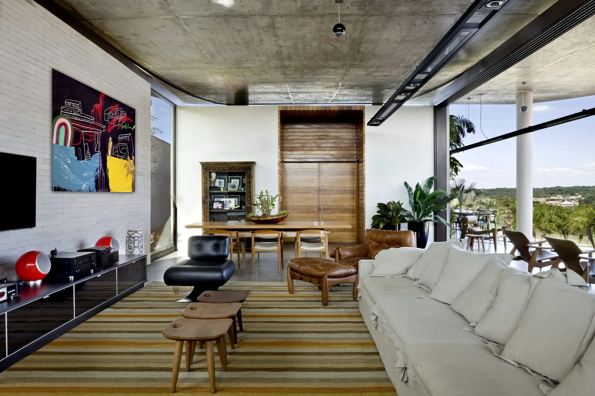 A spacious living room features an exposed concrete ceiling, a white brick wall with modern art, a striped rug, and a cream slipcovered sofa.