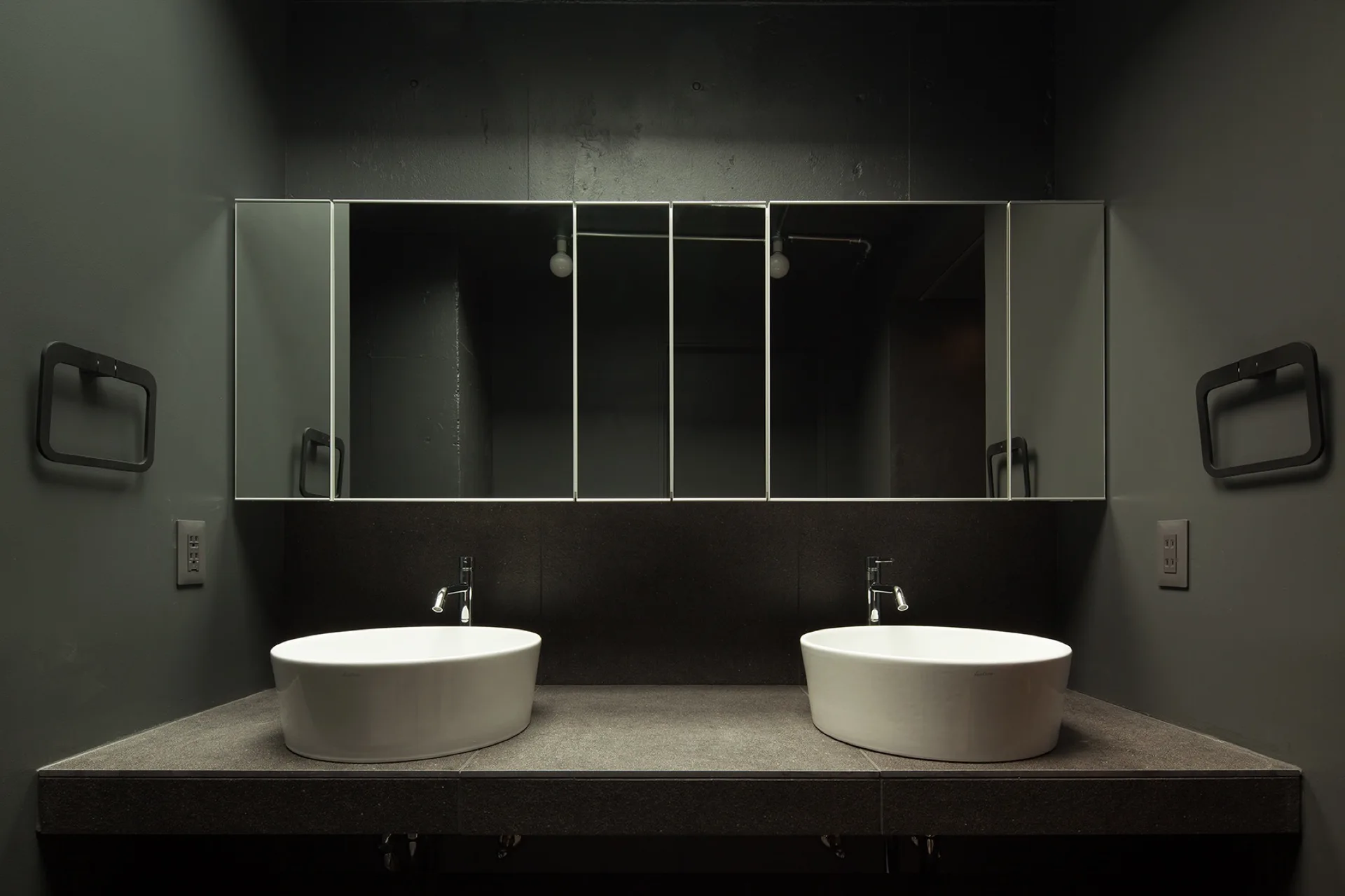 Symmetrical dark gray bathroom vanity featuring two white ceramic vessel sinks beneath a wide frameless mirrored cabinet.