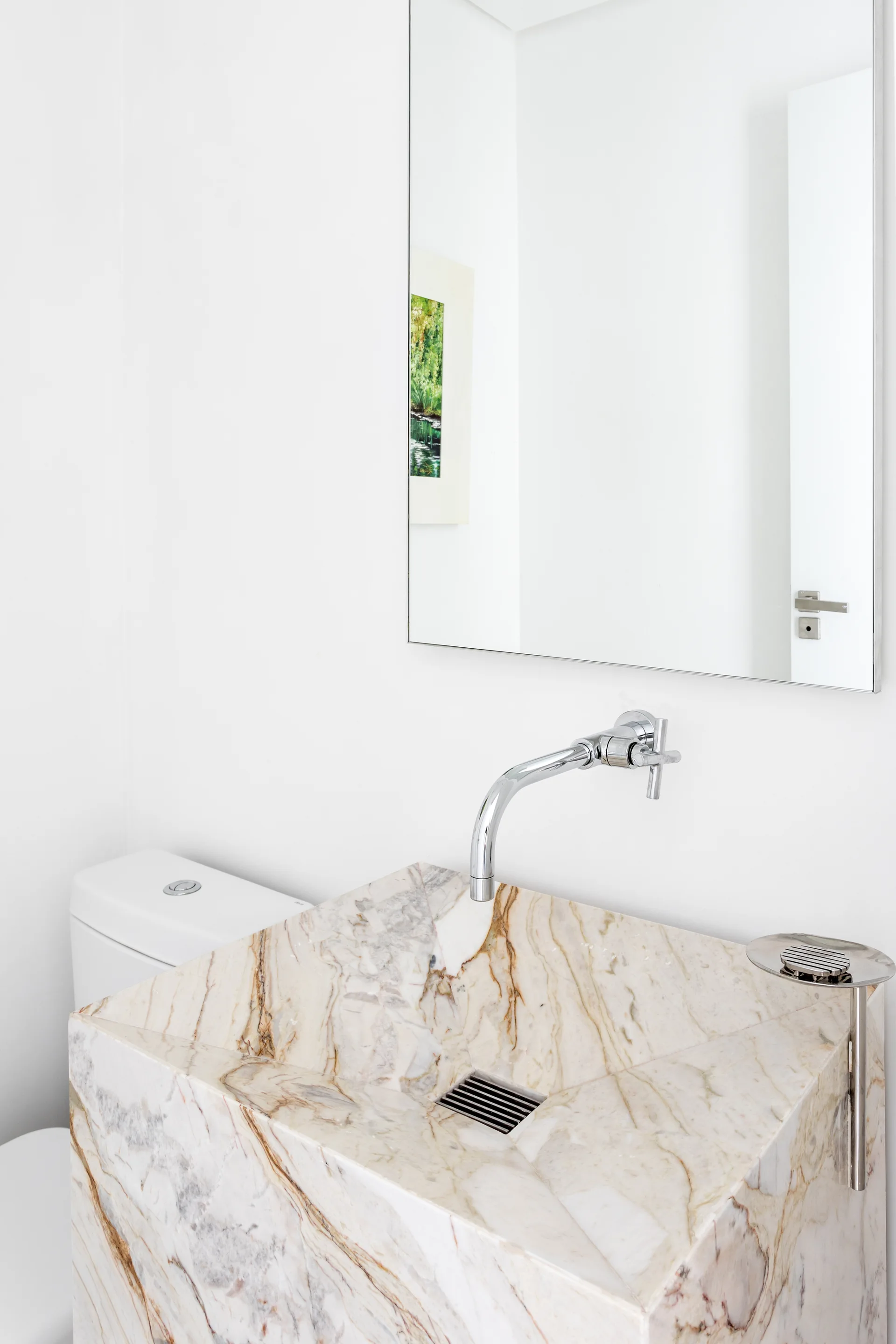 A minimalist white bathroom features a blocky marble sink with warm veining, a wall-mounted chrome faucet, and a frameless mirror.