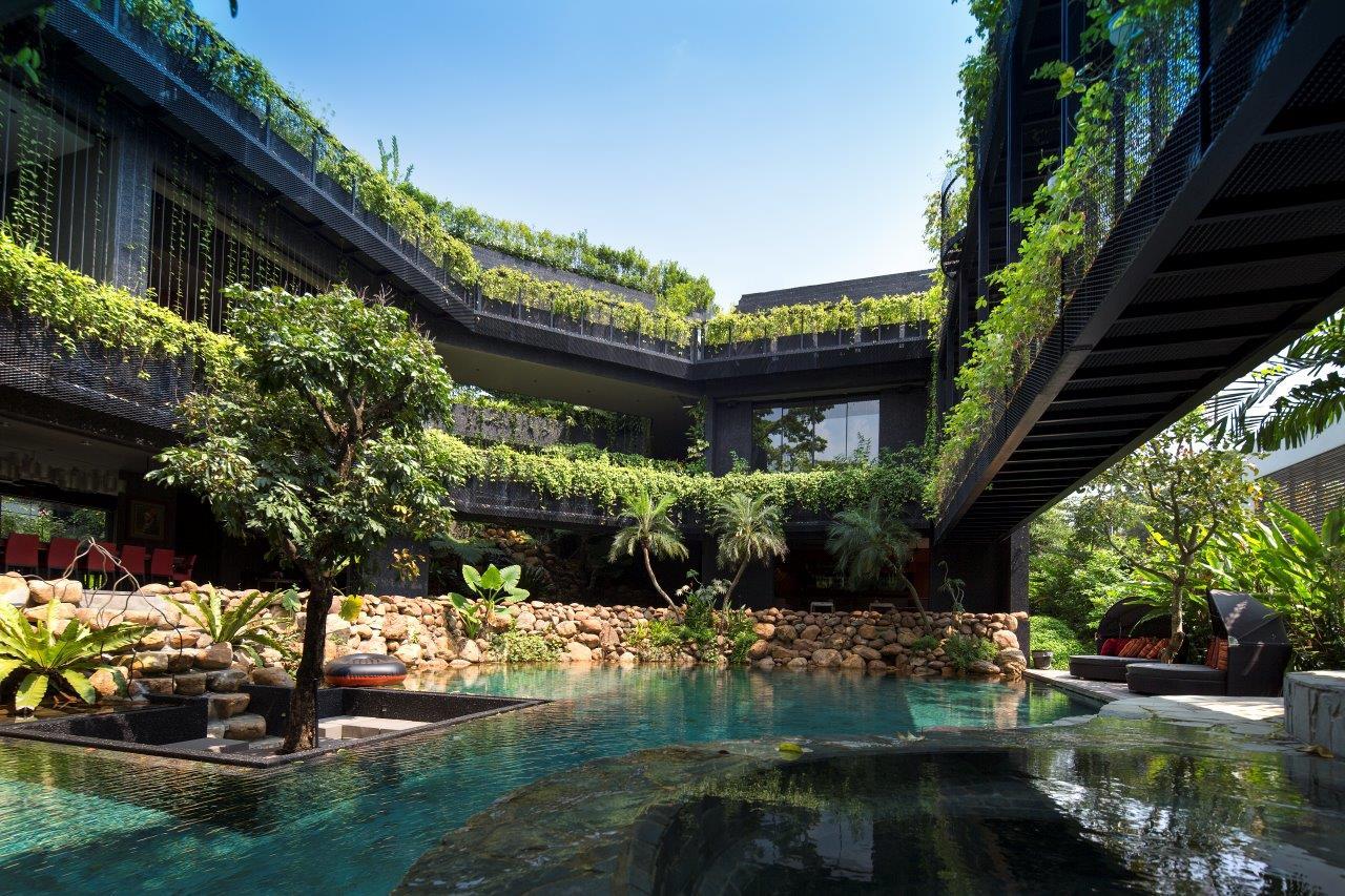 A modern multi-level courtyard with dark architectural structures, integrated green balcony planters, a swimming pool, and a stone retaining wall.