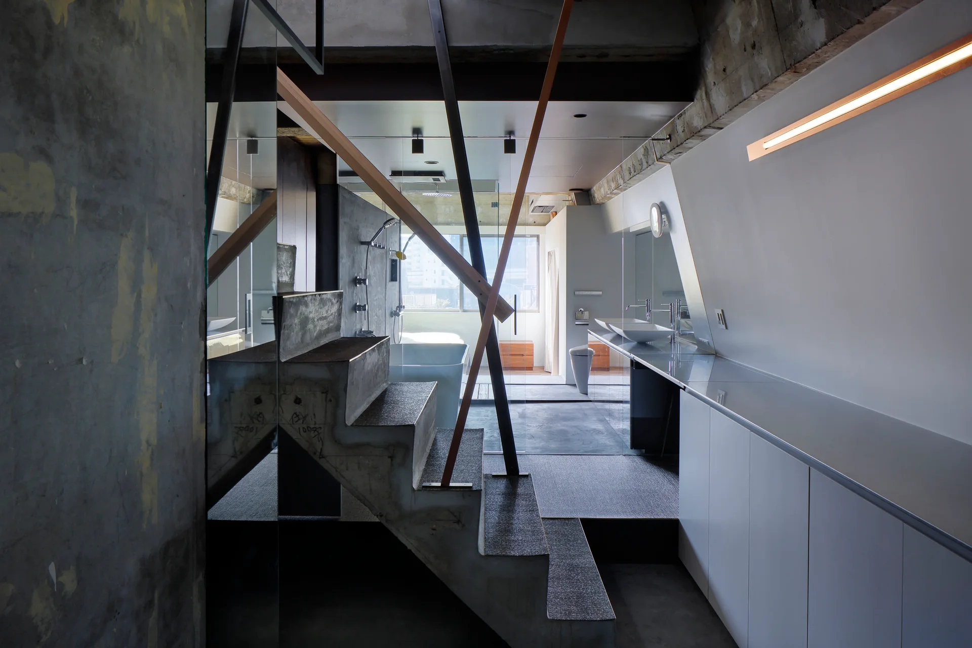 A minimalist industrial bathroom featuring a raw concrete staircase, a long white floating vanity with vessel sinks, and a glass partition.