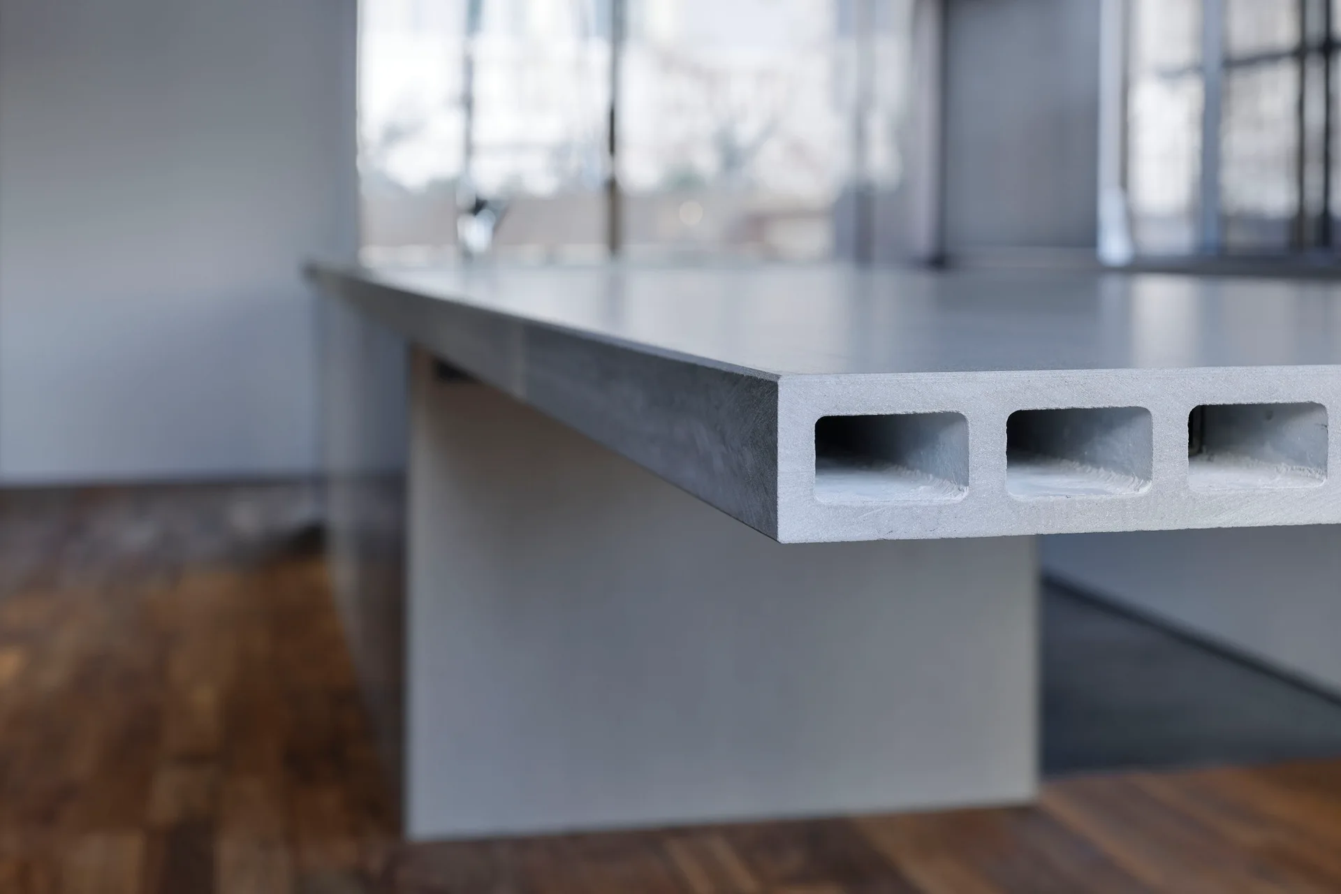 A close-up shot of a thick grey concrete countertop showing three hollow rectangular channels along its exposed side edge.