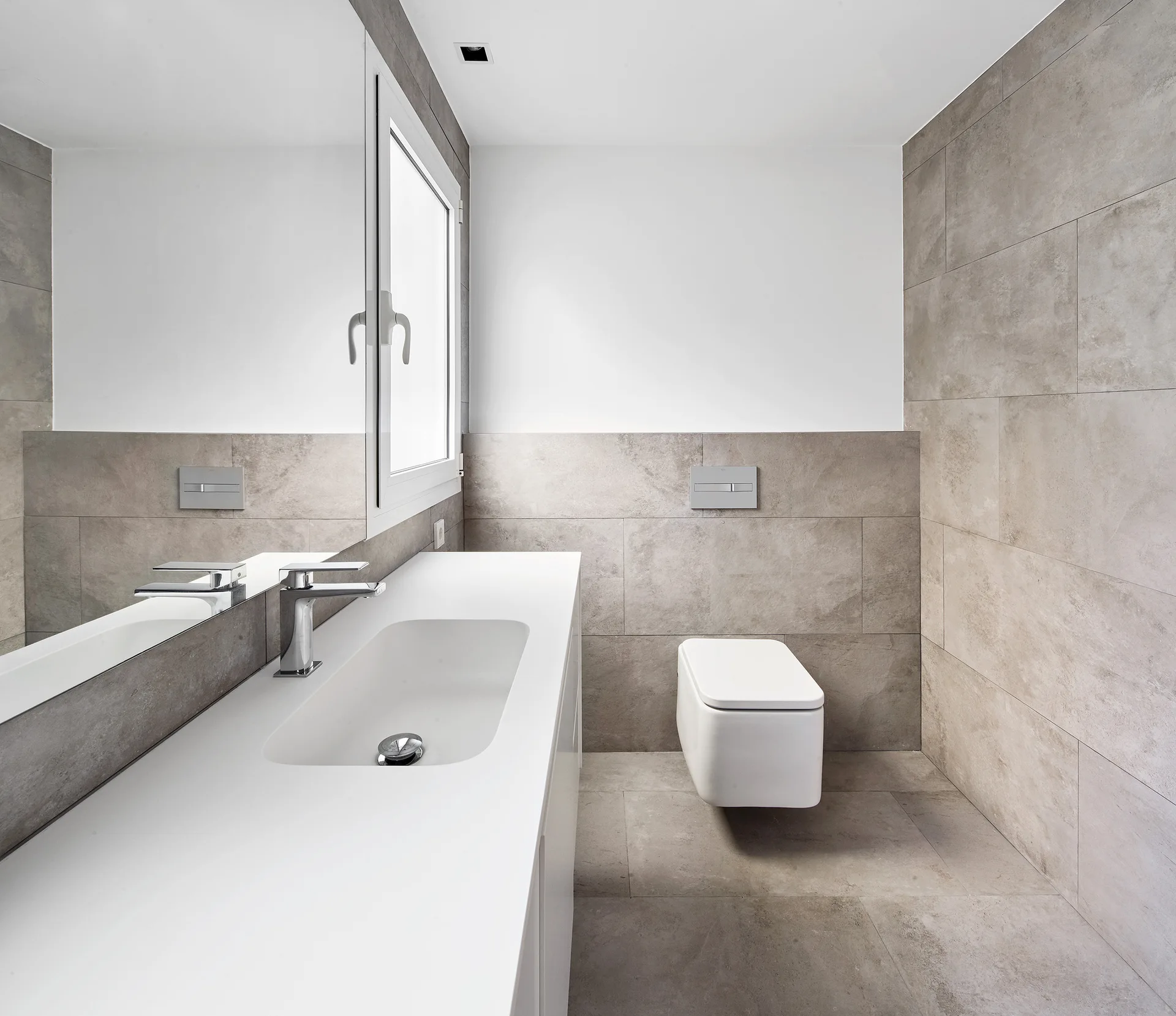 A contemporary bathroom with grey stone-look floor and wall tiles, a wall-mounted white toilet, and a seamless white integrated sink vanity.