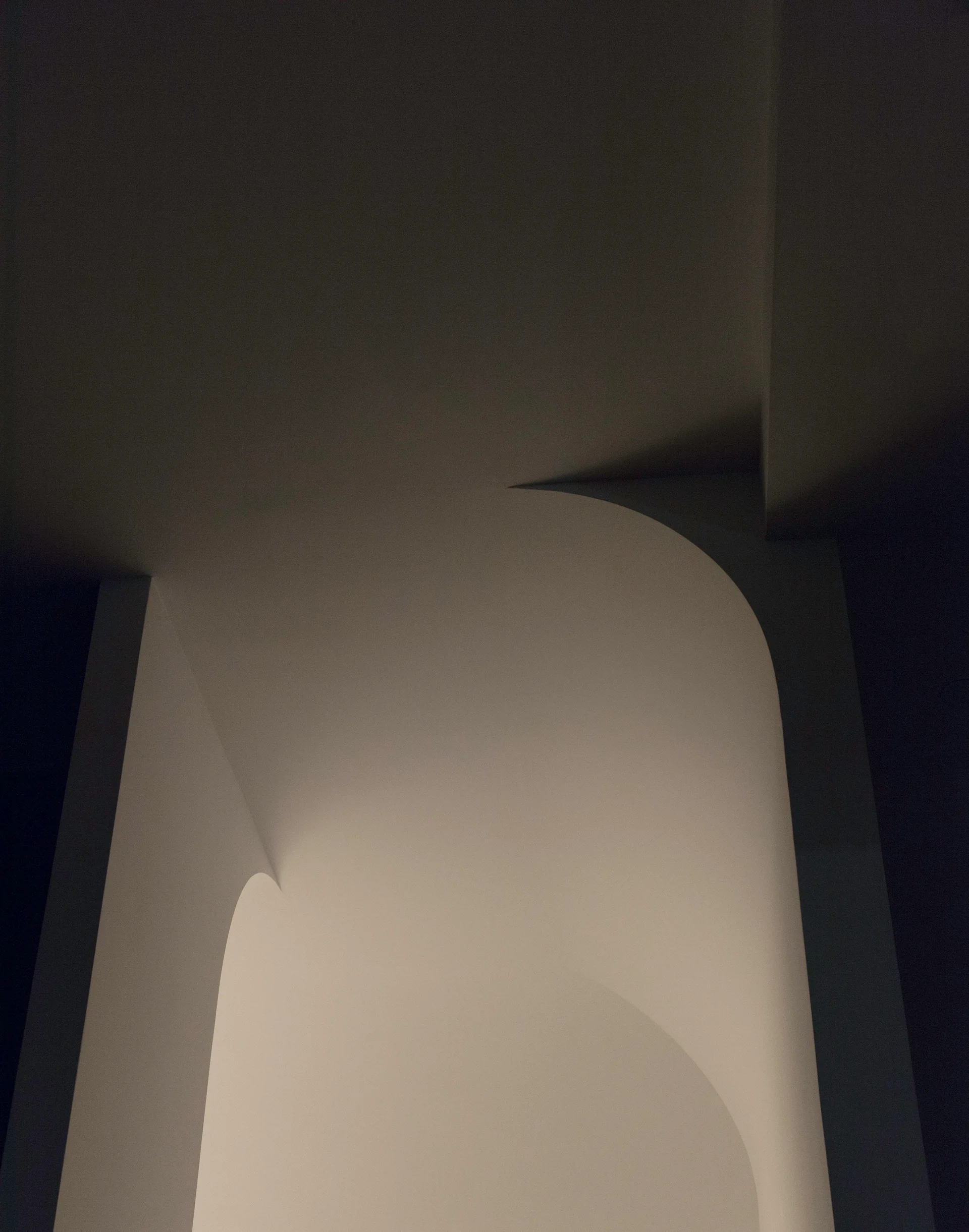 A close-up of a minimalist plaster archway with a smooth matte finish, showing sharp shadows and soft lighting on the curved architectural surfaces.