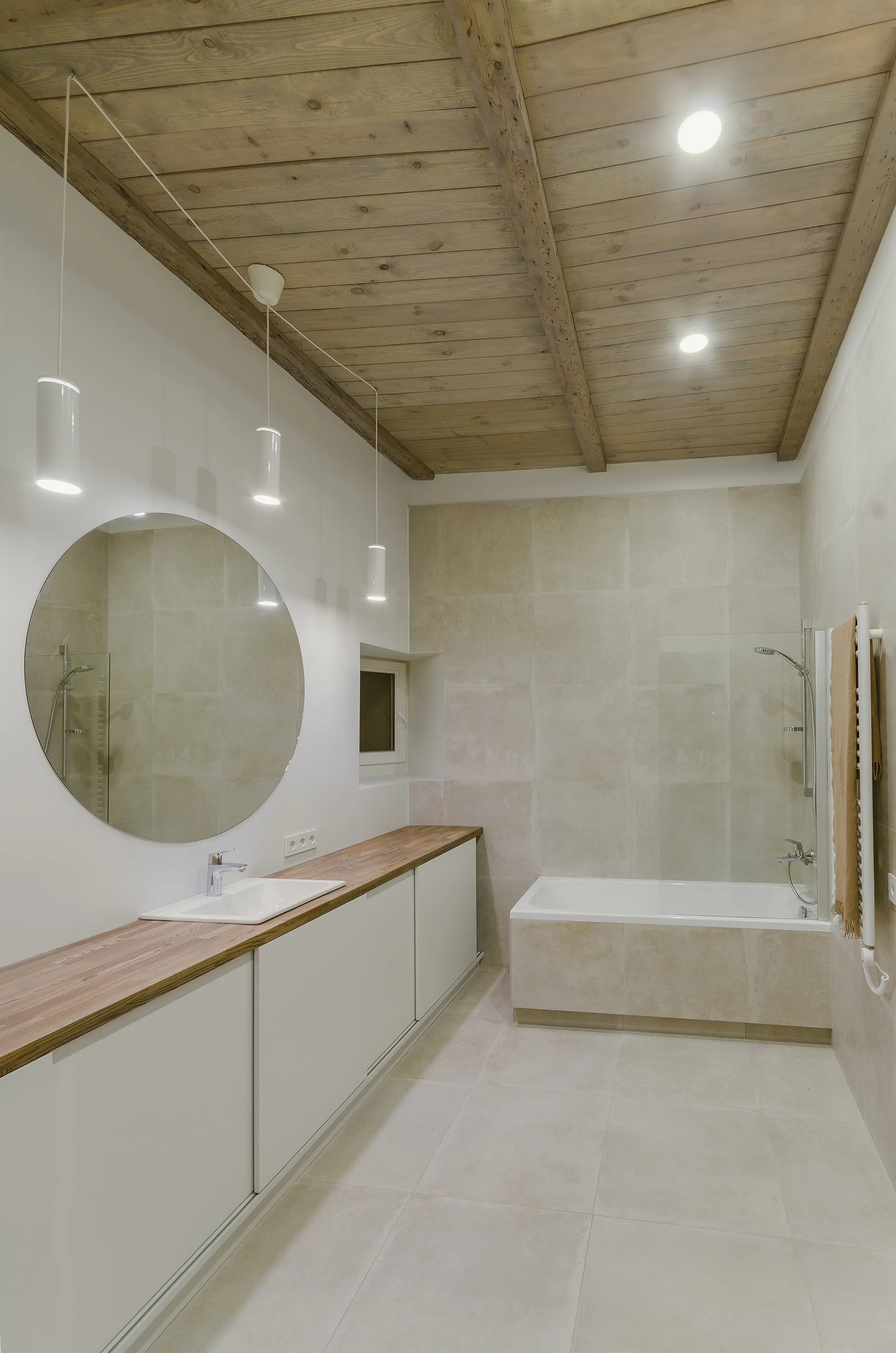 A modern bathroom featuring a long white vanity with a wood countertop, a round mirror, and a wood plank ceiling.