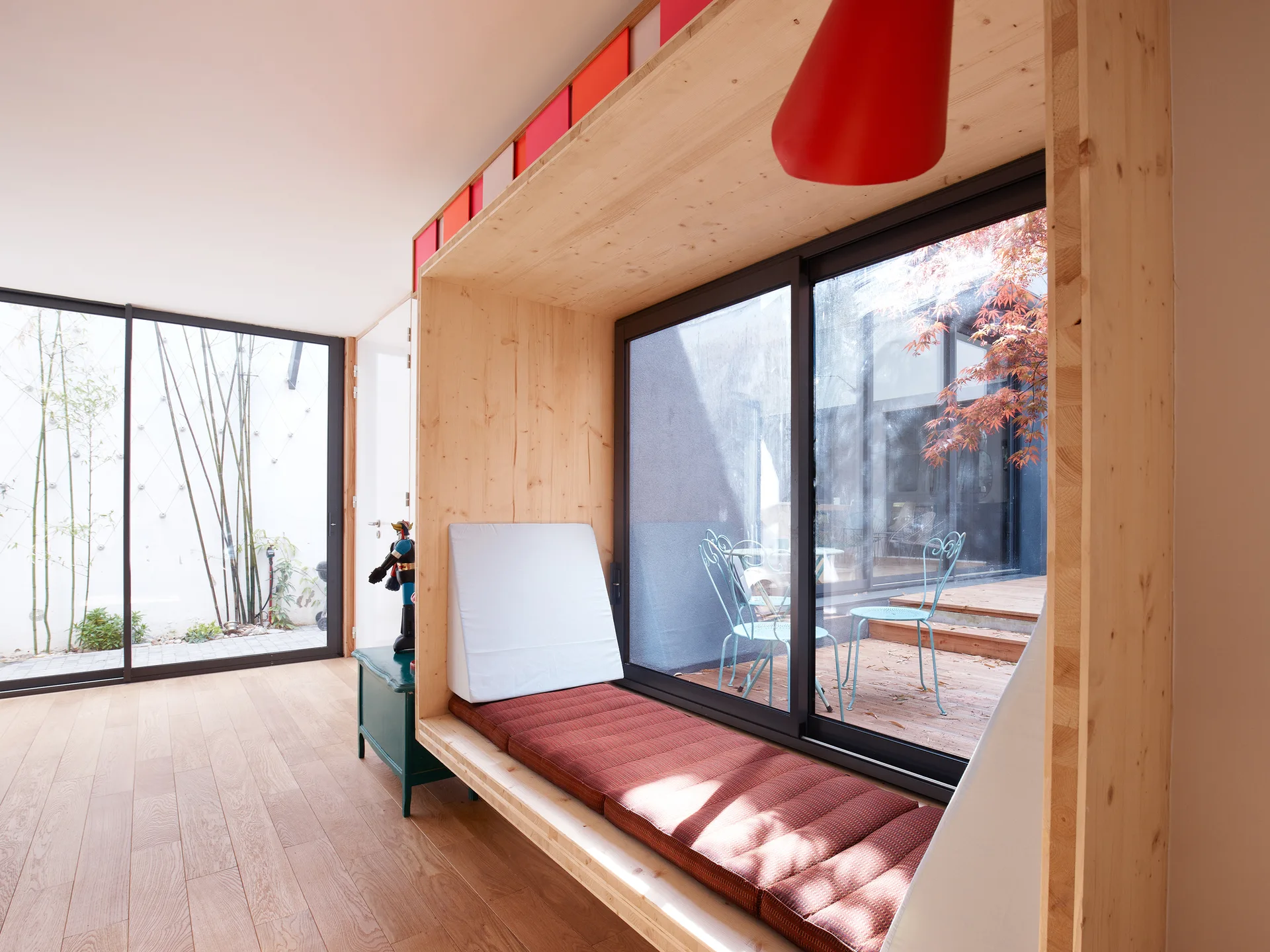 A built-in light wood window seat with a red cushion is set inside a deep wooden box framing next to a sliding glass patio door.