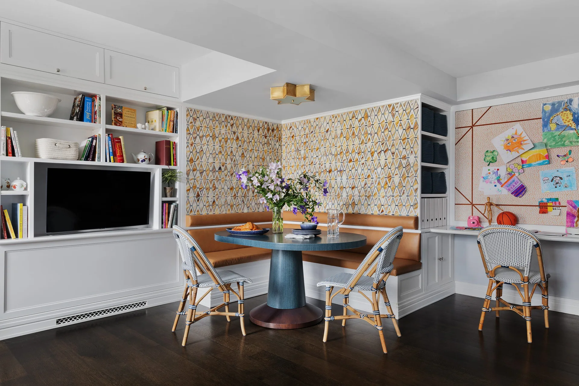 A breakfast nook features an L-shaped leather banquette, a blue round pedestal table with rattan bistro chairs, and geometric patterned wallpaper.