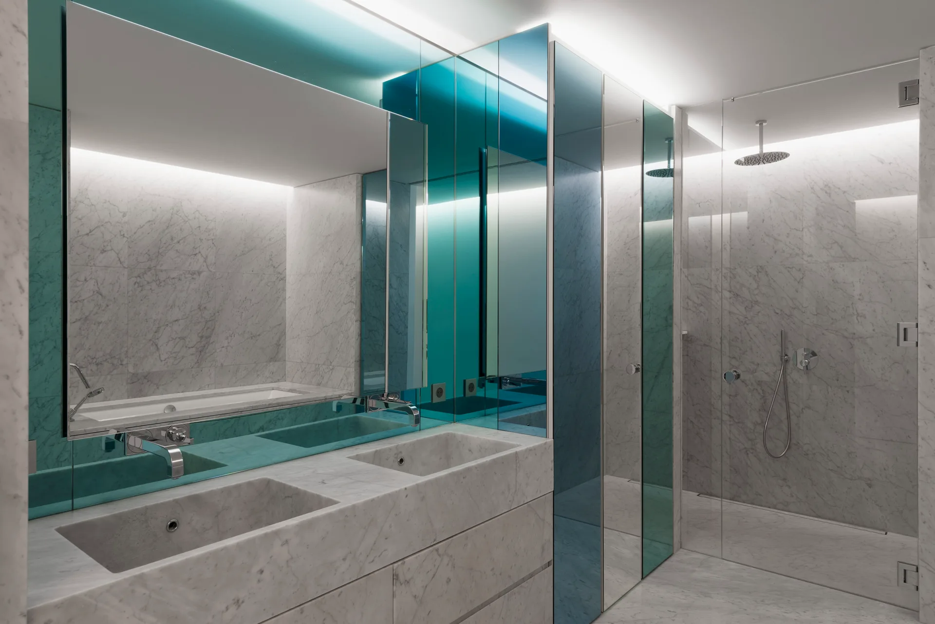 A modern bathroom with a white veined marble vanity, wall-mounted faucets, a glass shower enclosure, and blue-tinted mirror panels.
