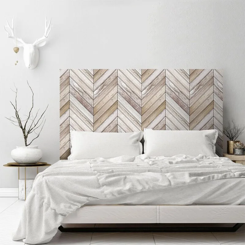 A bed with white bedding and pillows features a large wall-mounted wood headboard with a herringbone pattern against a white wall.