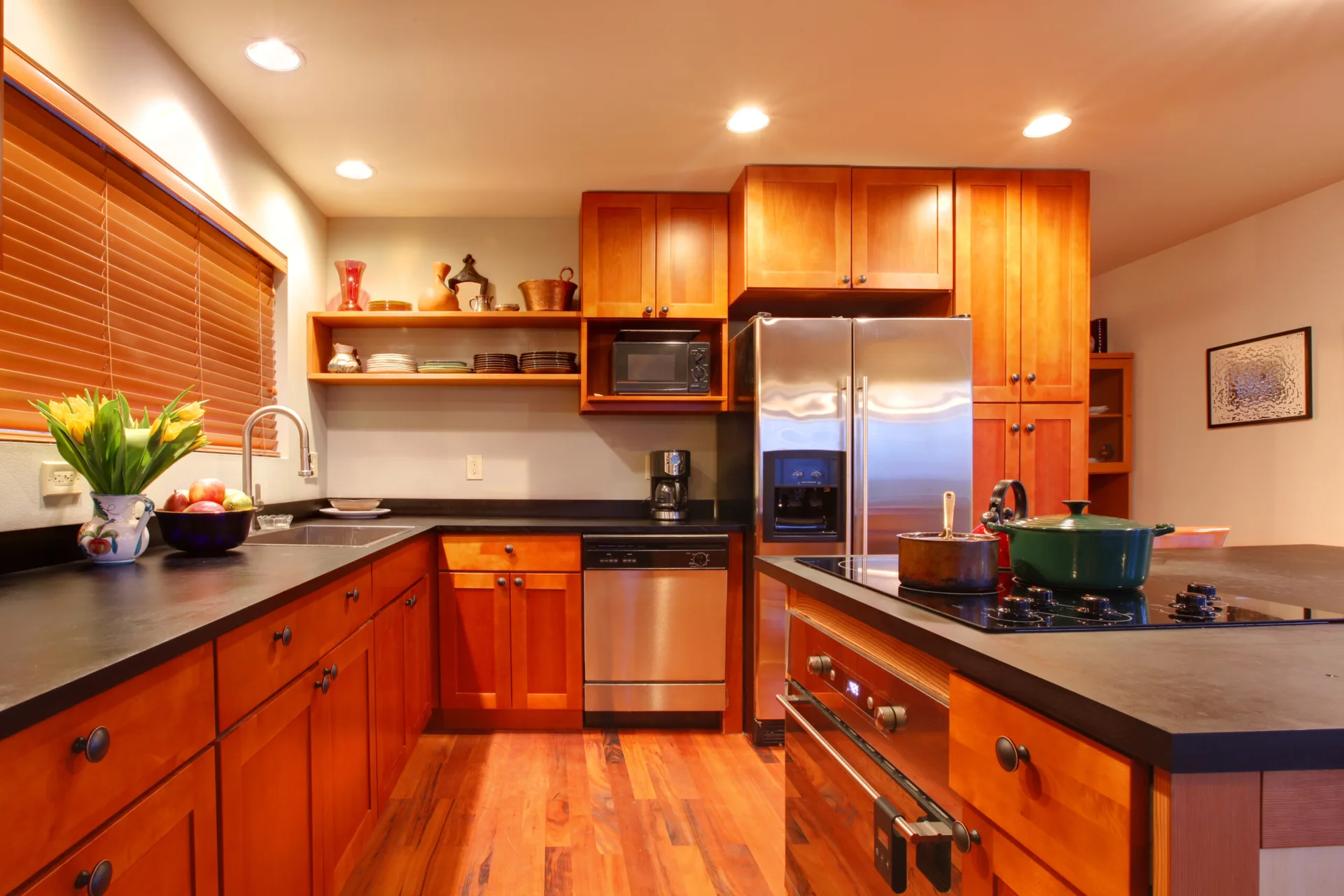 A kitchen with warm cherry wood cabinets, black countertops, stainless steel appliances, and a wood floor.