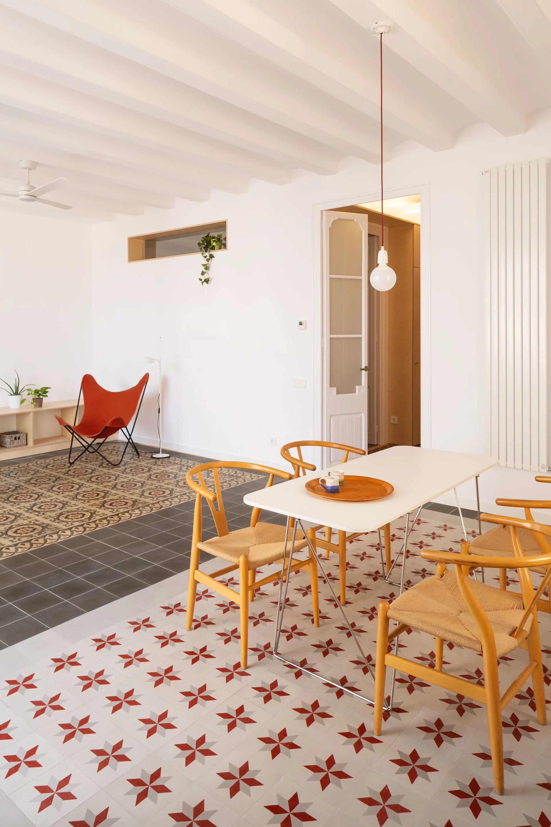 A bright dining area featuring a white table and light wood wishbone chairs on red and white star-patterned floor tiles.