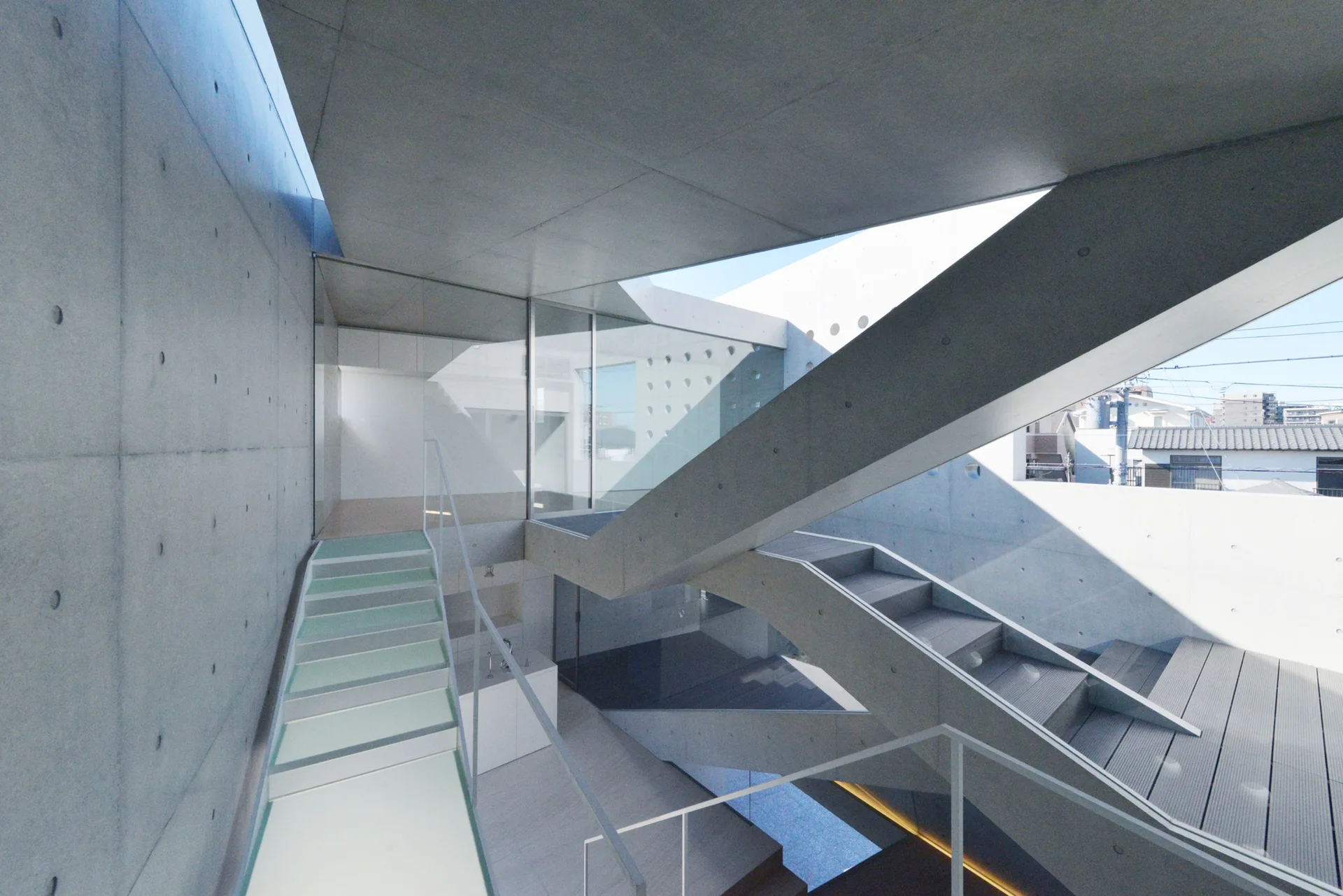 A multi-level concrete staircase with angular geometries, glass walls, and thin white railings in an open architectural space.