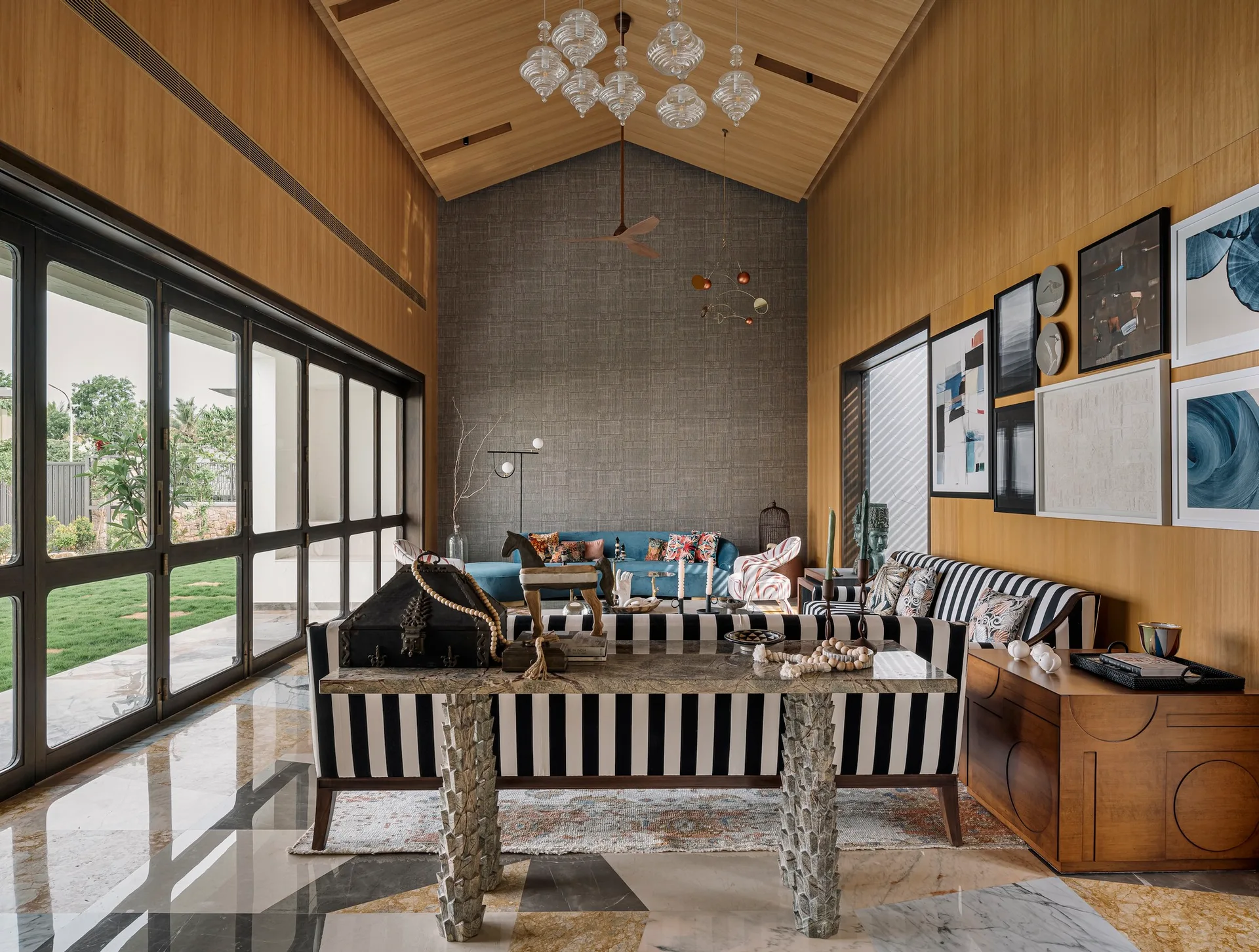 A spacious living room with a wood-paneled vaulted ceiling, a black and white striped sofa, a stone console table, and large glass doors.