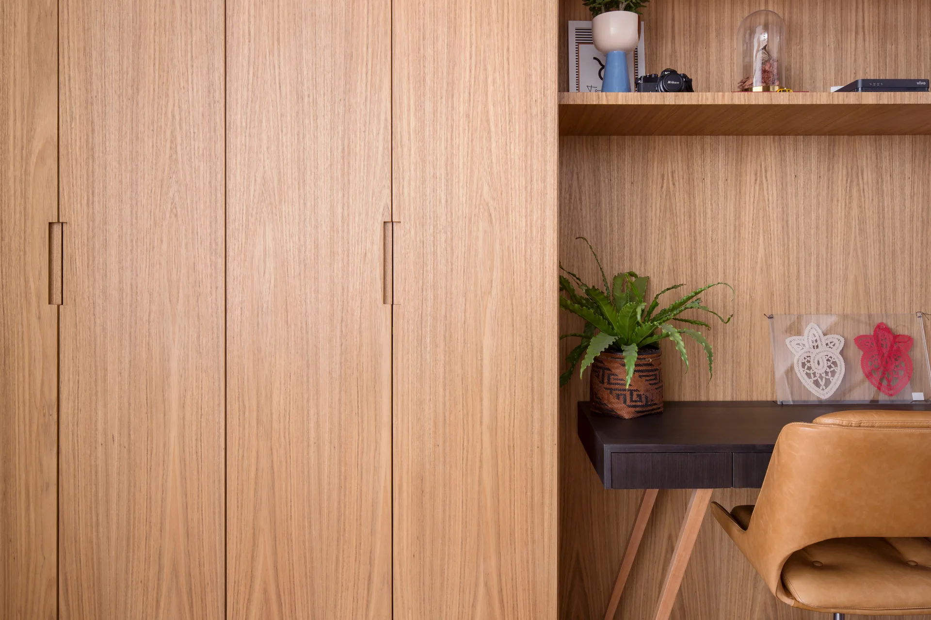 A custom light wood storage wall with integrated cabinetry and shelves framing a dark desk with a tan leather chair.