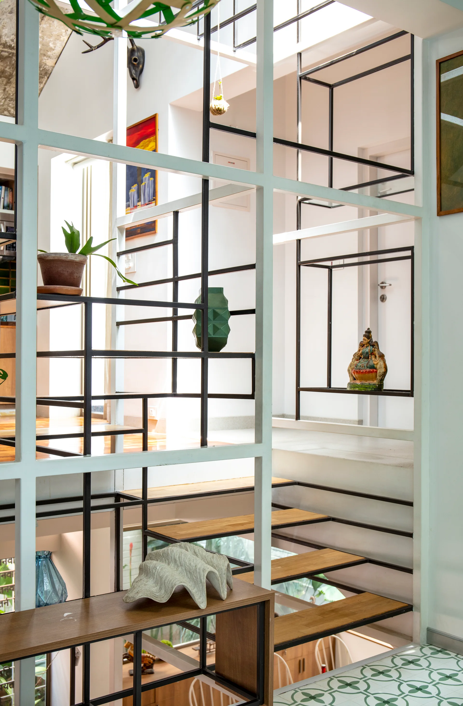 An open wooden staircase features a white metal grid room divider displaying a green vase, a shell sculpture, and other decorative objects.
