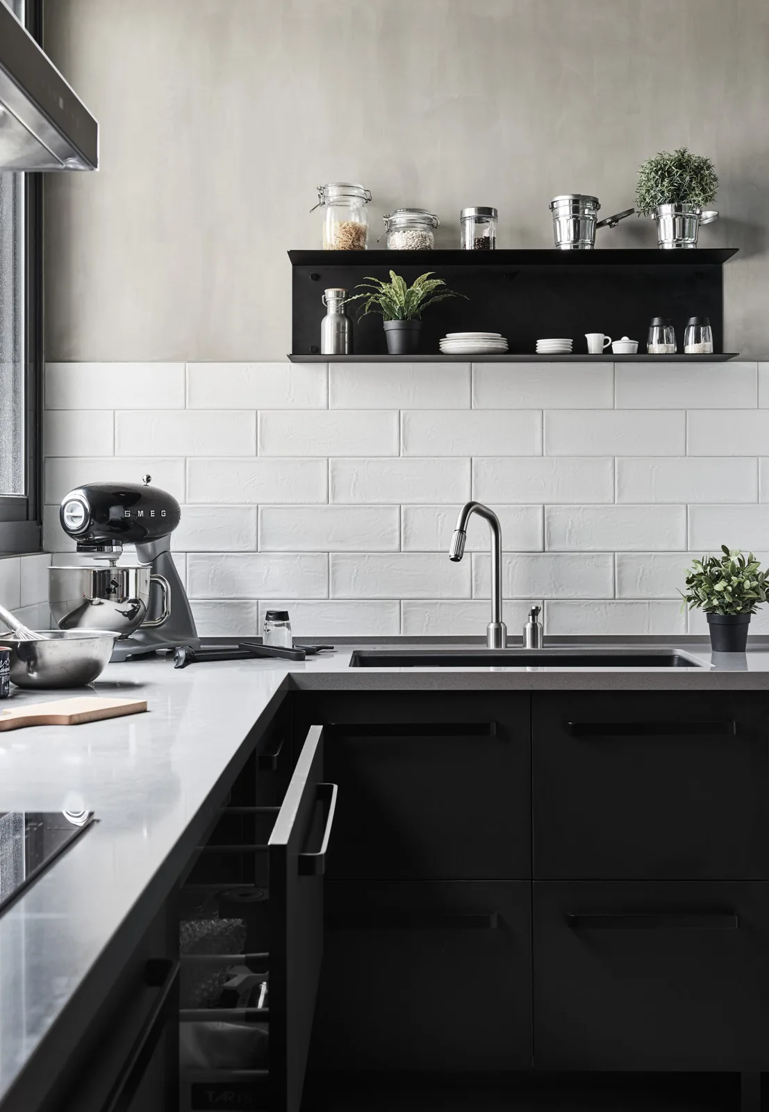 A modern kitchen sink area with matte black cabinets, grey solid surface countertops, a white subway tile backsplash, and a black wall shelf.