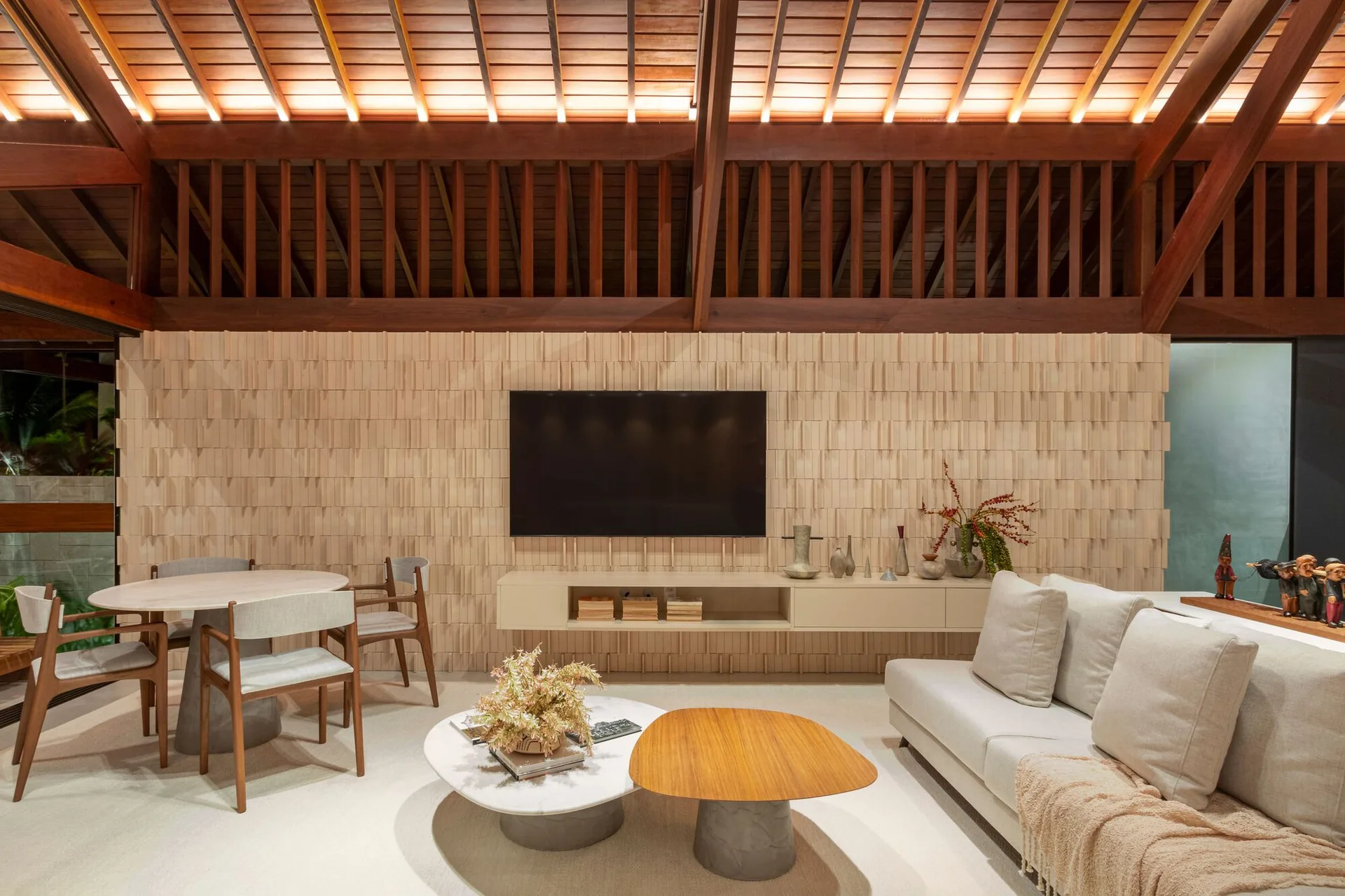 A spacious living area featuring a textured wood-shingle accent wall, a floating media console beneath a TV, and a high pitched ceiling with wooden beams.