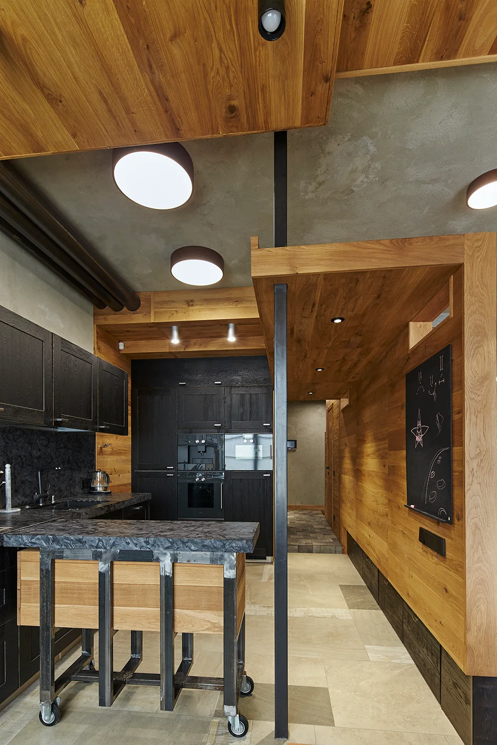 An industrial kitchen featuring dark wood cabinets, a rolling wooden island, and warm timber wall cladding beneath a raw concrete ceiling.