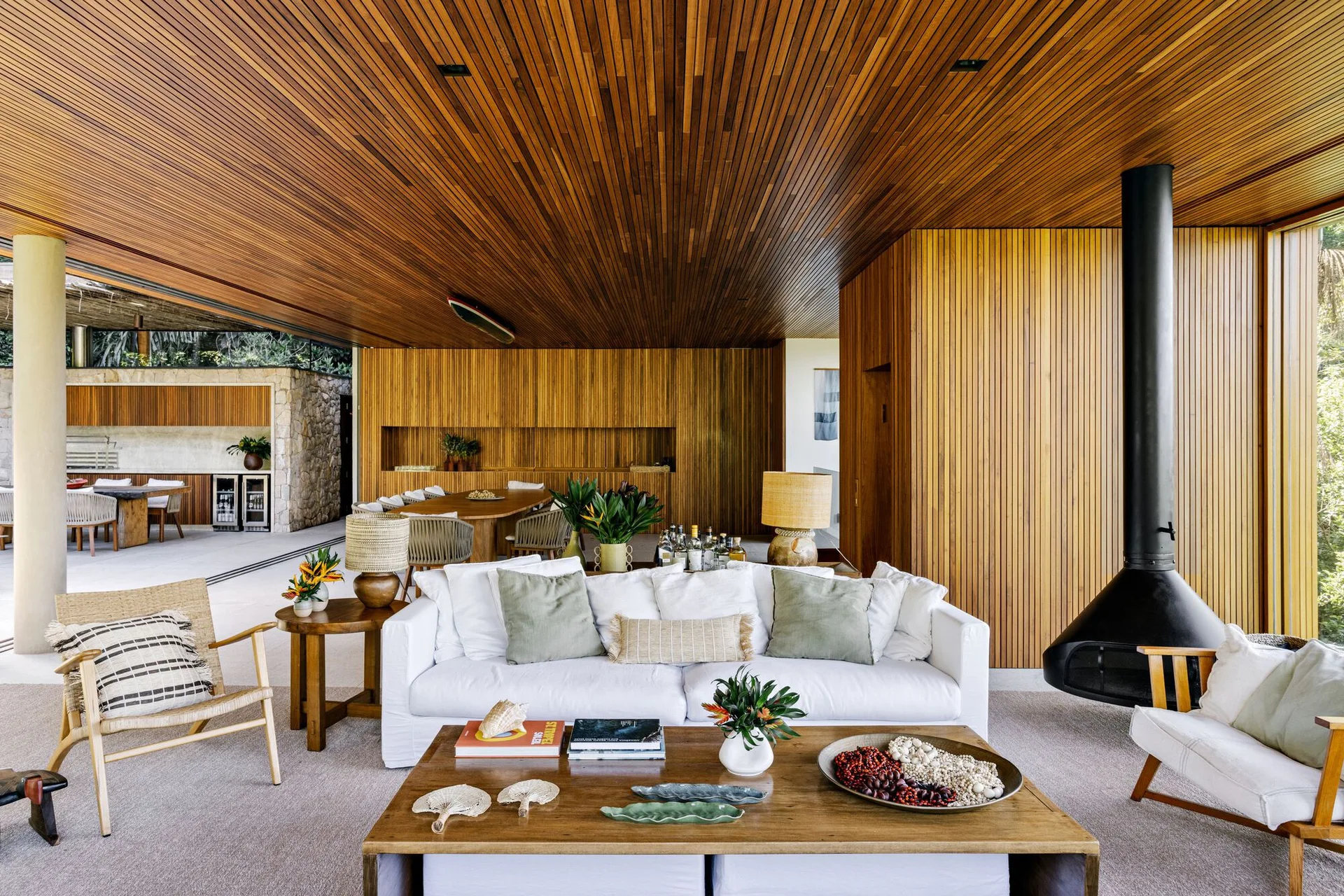 An open living space features wood slat walls and ceiling, a white sofa, a wooden coffee table, and a black suspended fireplace.
