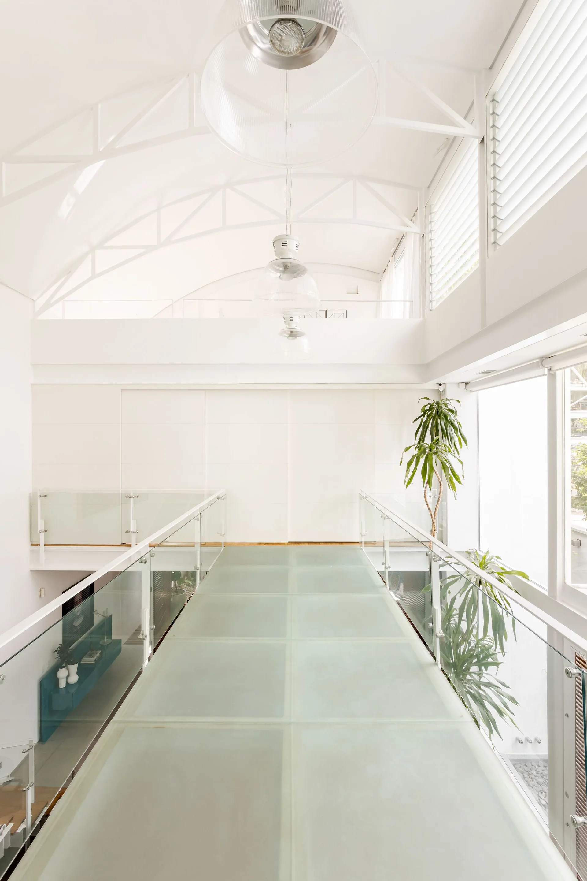 An elevated interior walkway features frosted glass floor panels and transparent glass railings under a high vaulted white ceiling.